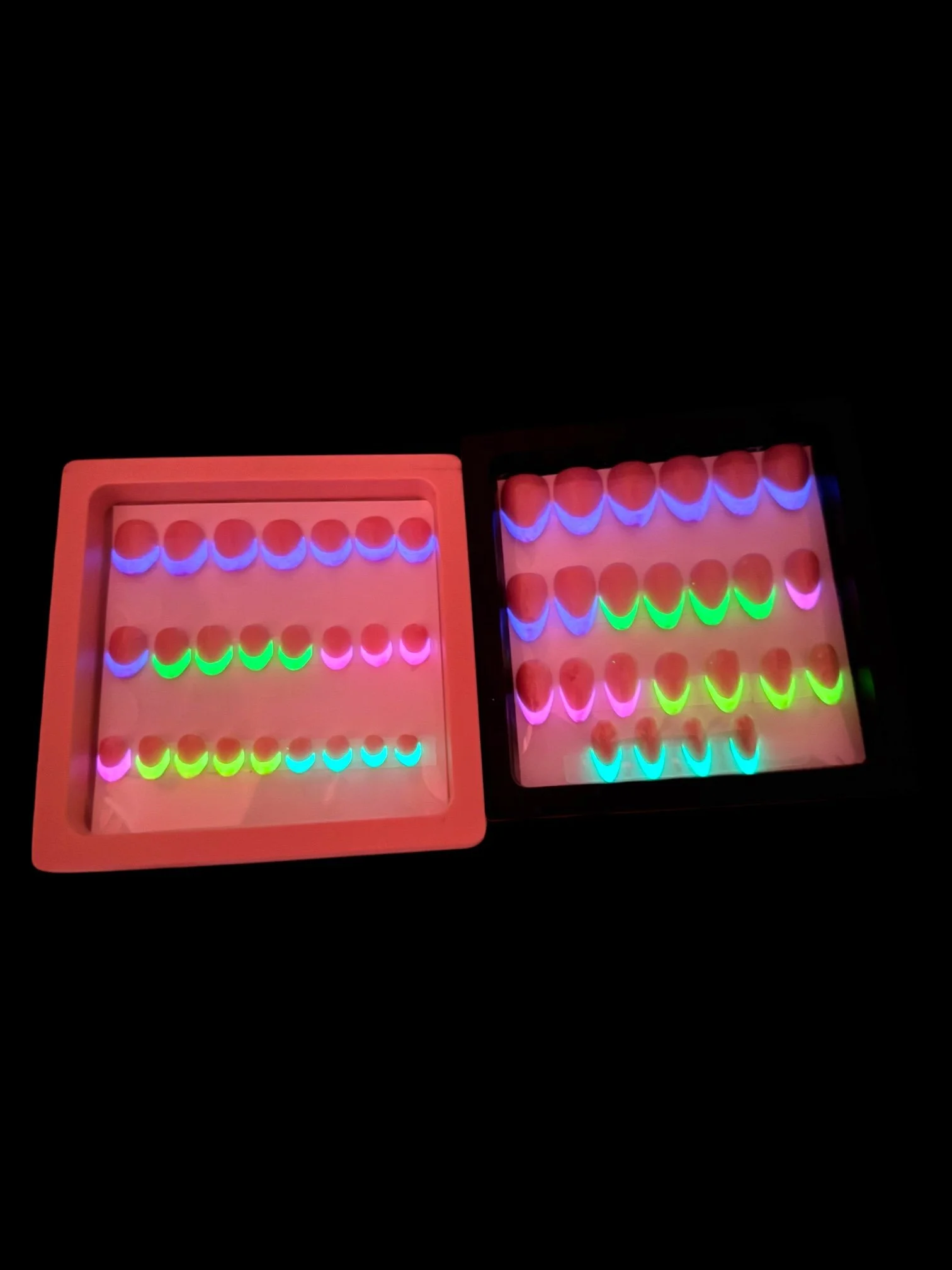 glowing Glow-in-the-dark almond press-on nails with nude pink bases and colorful neon rainbow French tips in purple, green, pink, yellow, and blue.