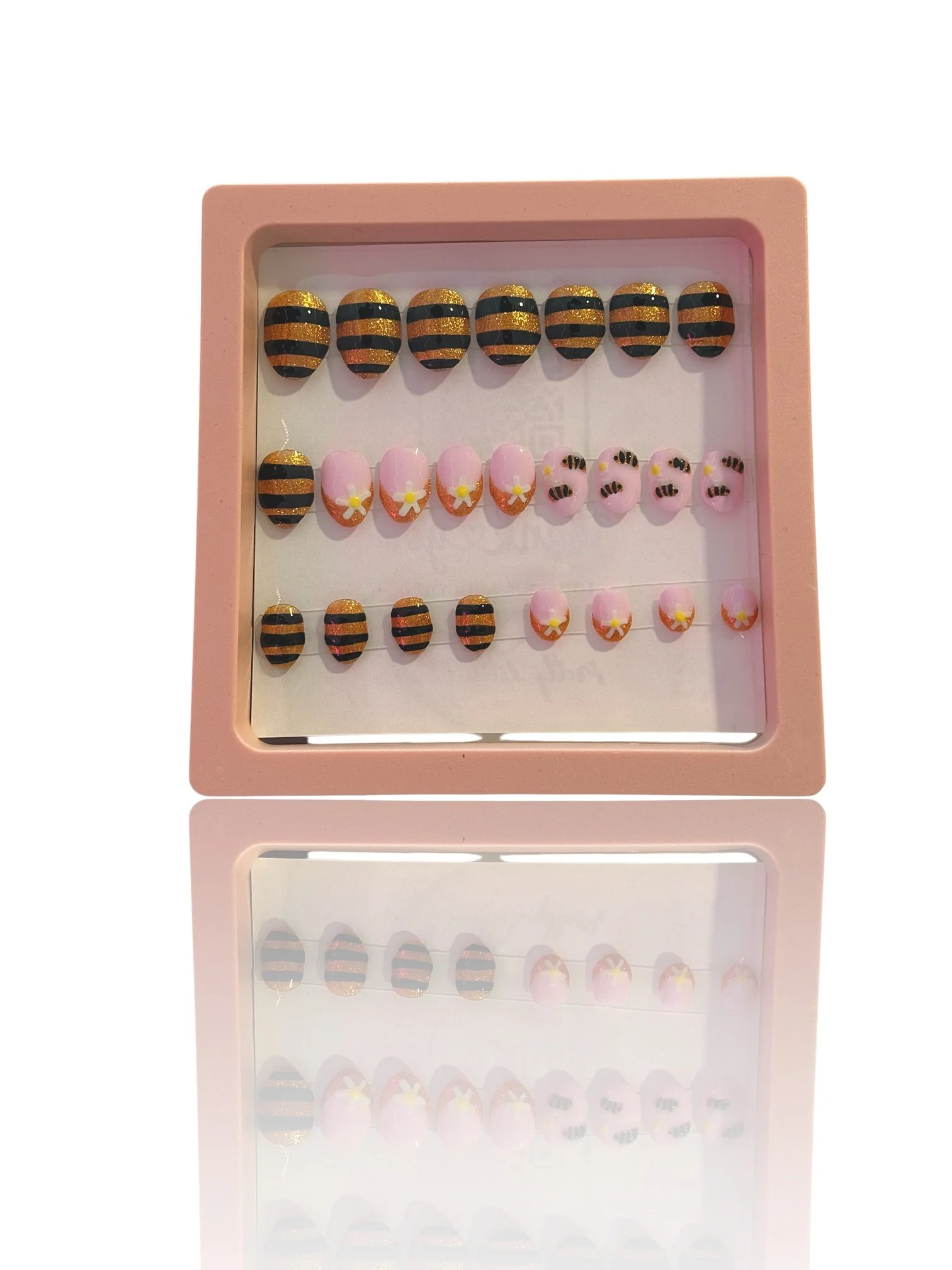 kids Glow-in-the-dark almond press-on nails with glittery orange and black bee stripes, pink bases, and cute bumblebee designs.