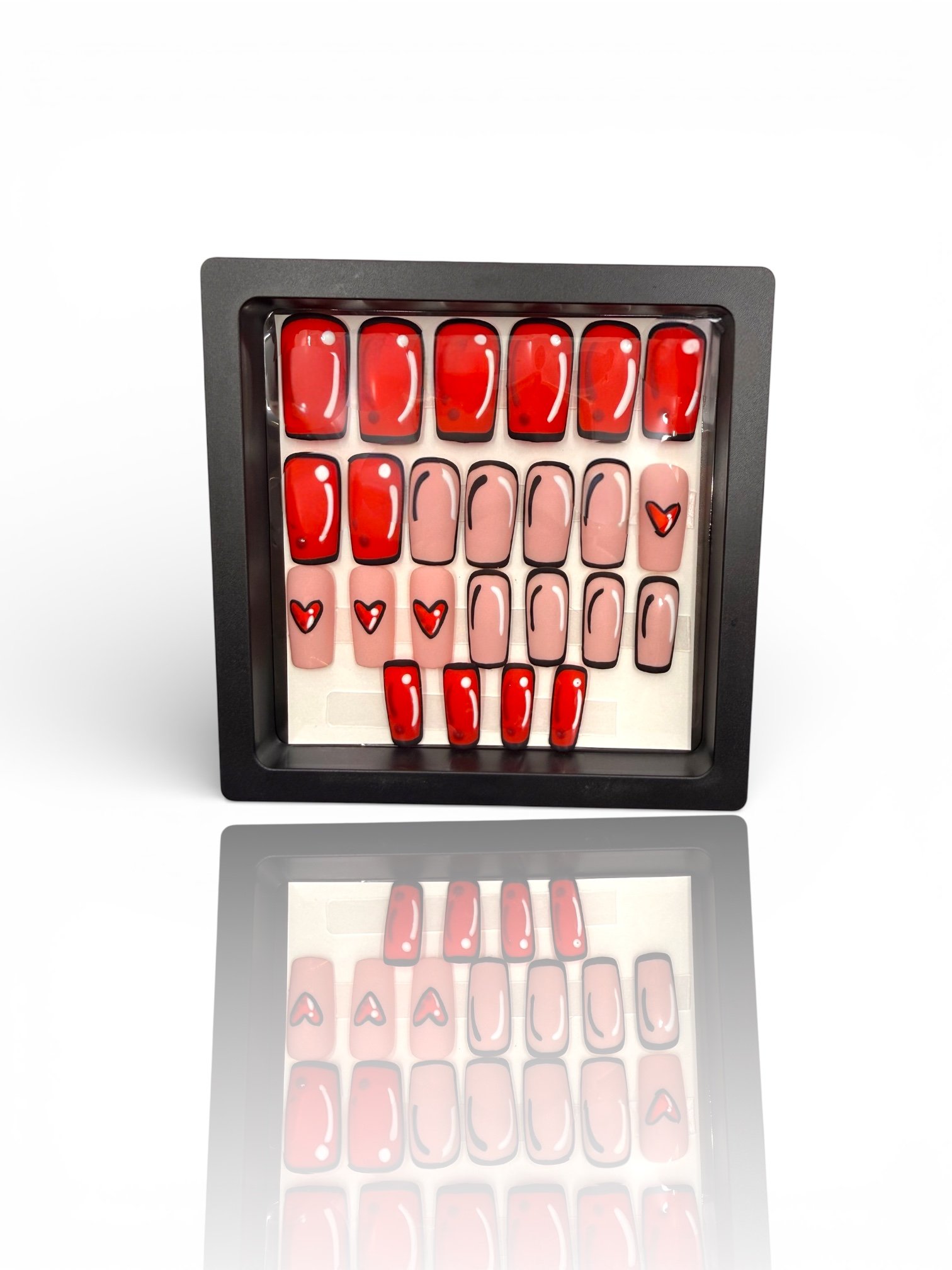 A black box containing rows of artificial nails with red, pink, and white designs, including hearts and black outlines.