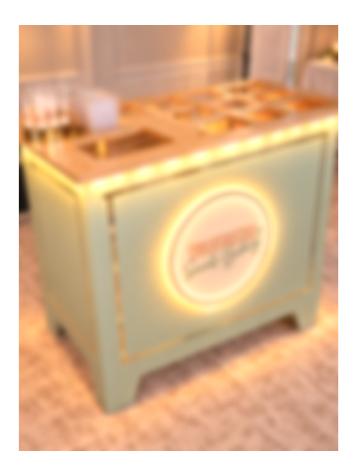 Blurry image of a brightly lit ice cream or dessert stand with a circular logo on the front.