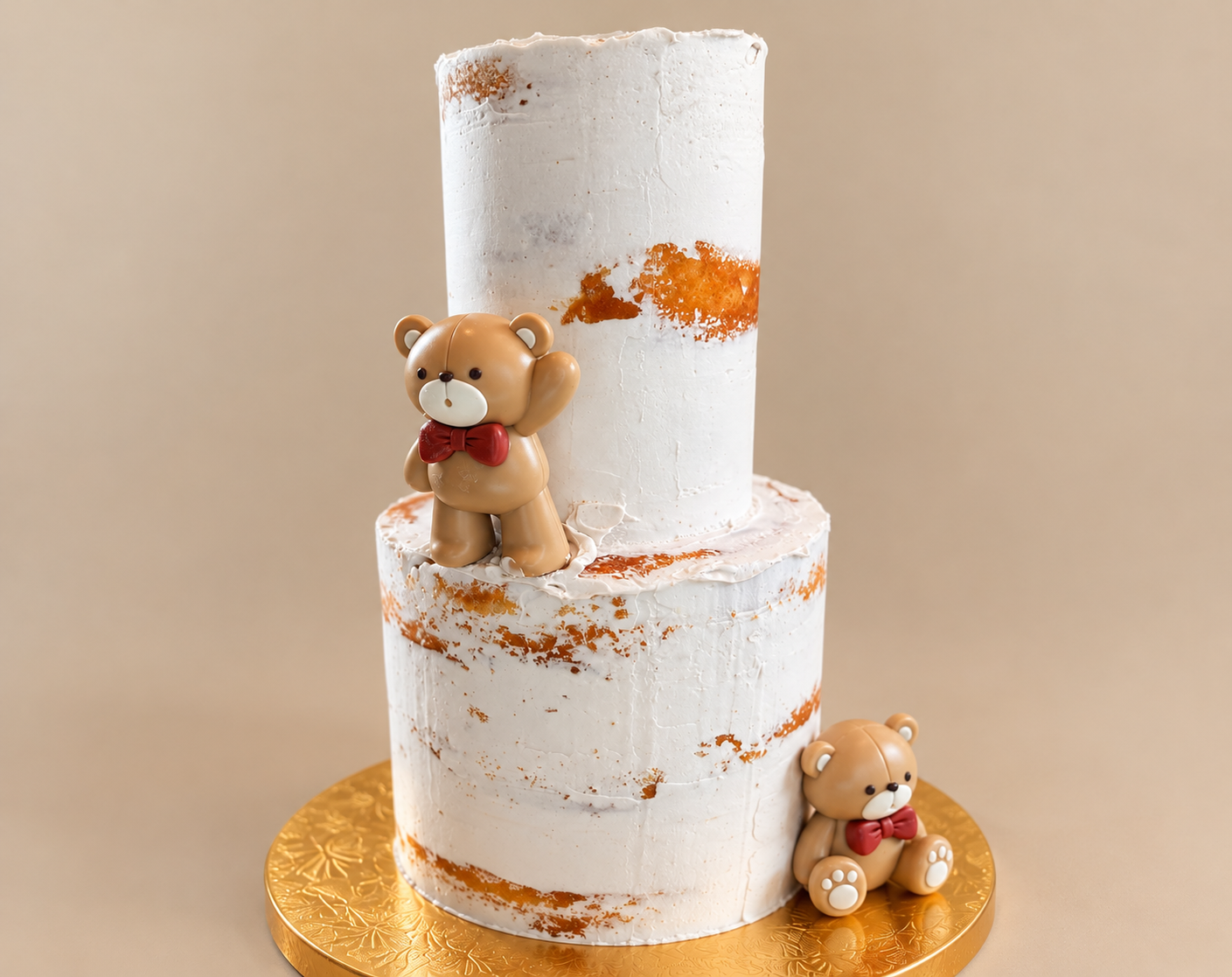 Two-tiered white cake with orange accents, decorated with two teddy bear figurines, one standing on the upper tier and one sitting on the lower tier, both wearing red bows, on a golden cake board.