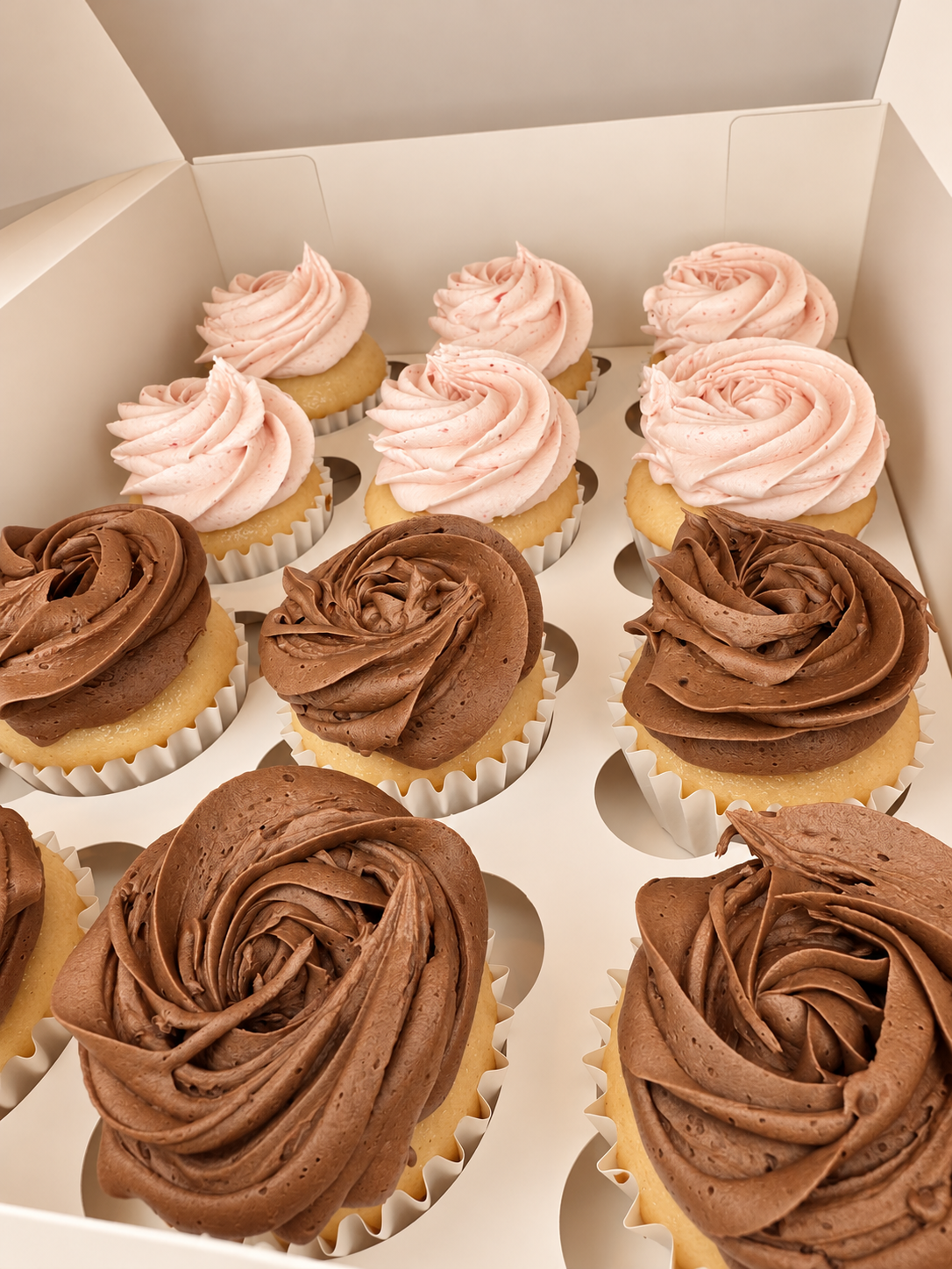 Three chocolate and six vanilla frosted cupcakes in white paper liners inside a white bakery box.