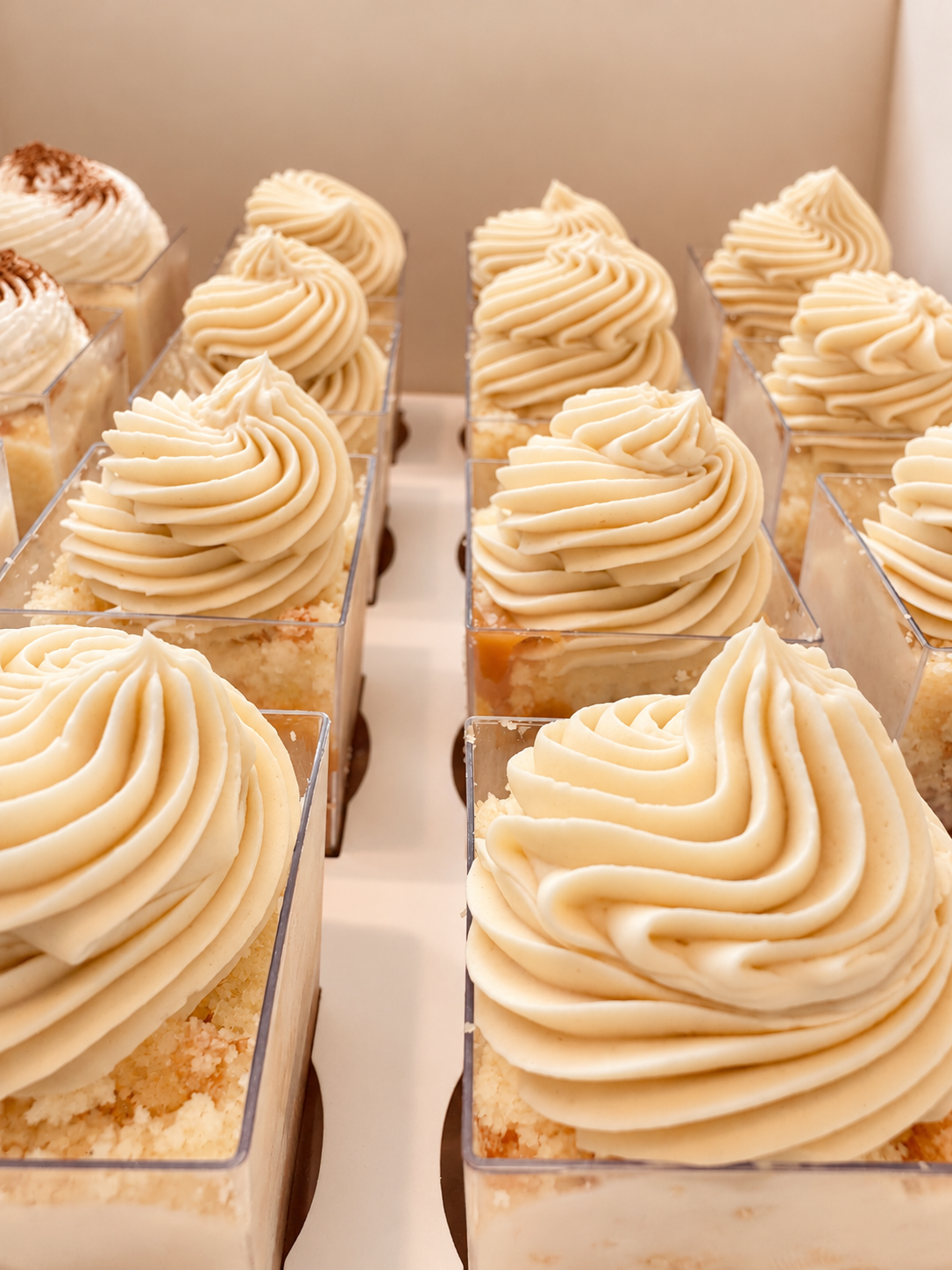 Close-up of individual layered dessert cups with cream topping and crumb crust layers inside clear plastic containers.