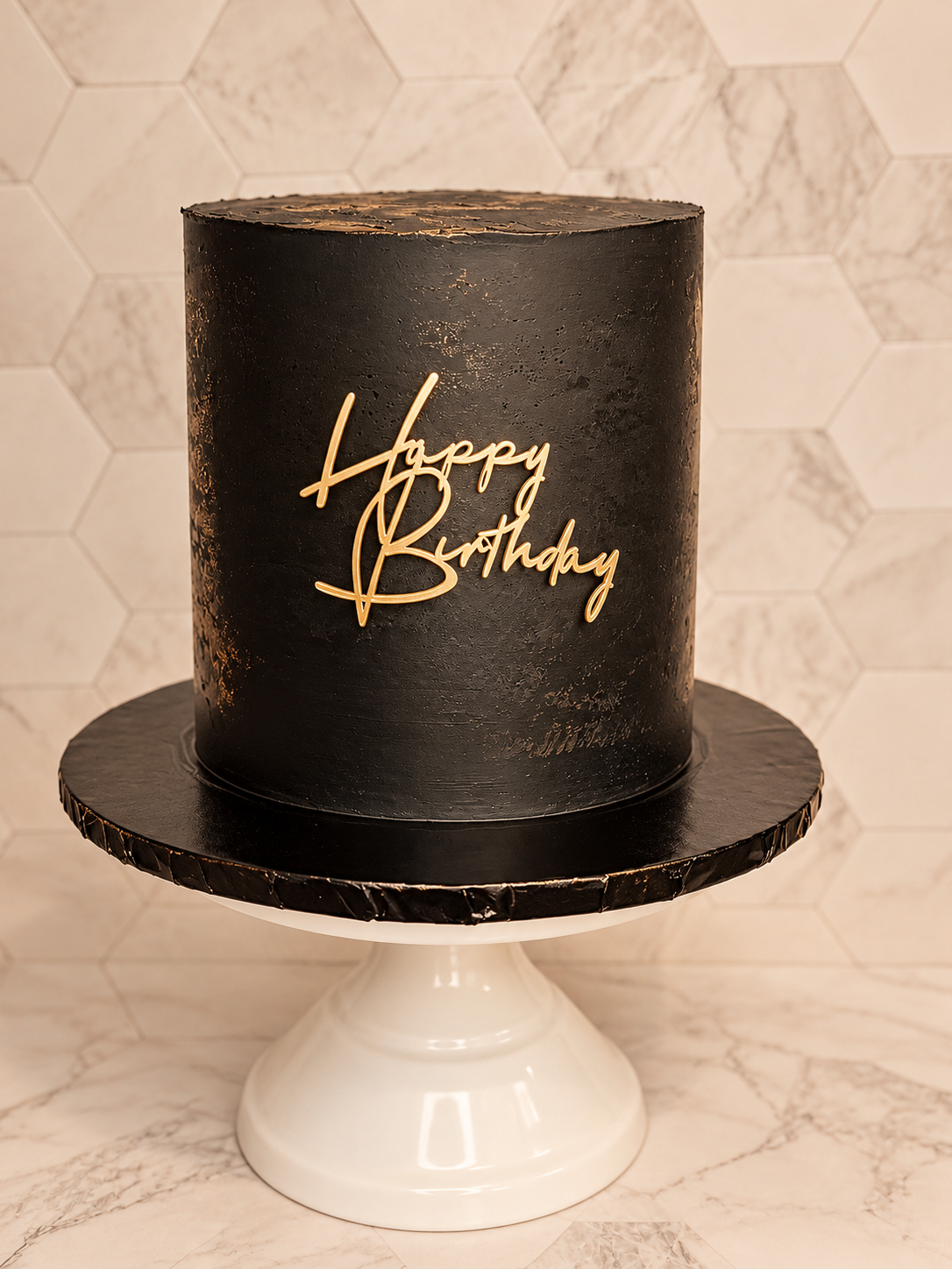 Black birthday cake with a neon 'Happy Birthday' sign on it, placed on a white cake stand with a hexagonal marble tile background.