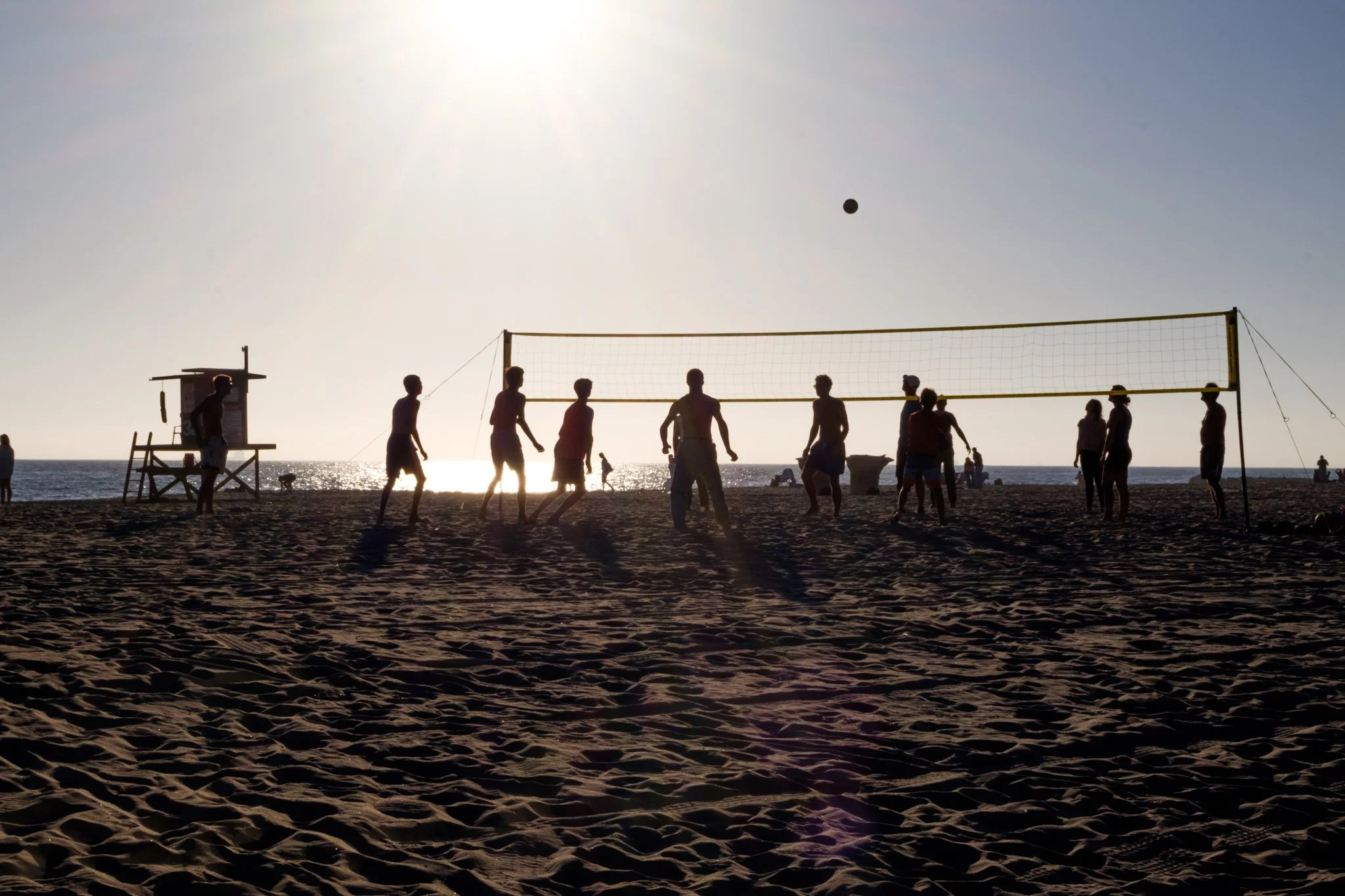 Silhouette of children playing volleyball on a beach during sunset with the ocean in the background.