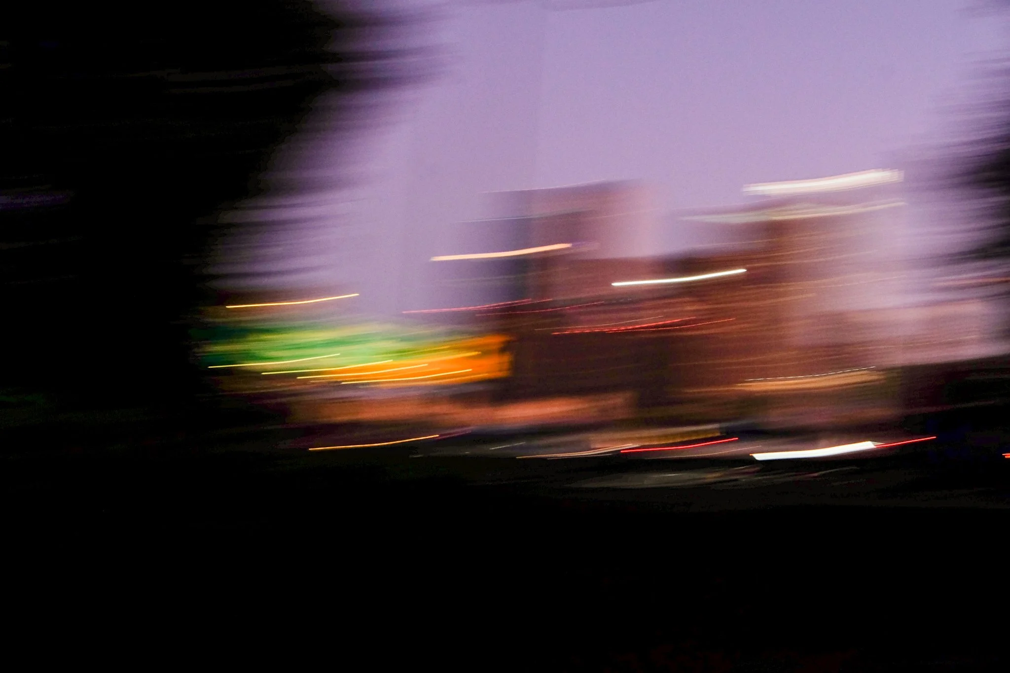 A blurry night scene with streaks of colorful lights and a purple sky, likely captured with a long exposure or intentional camera movement.