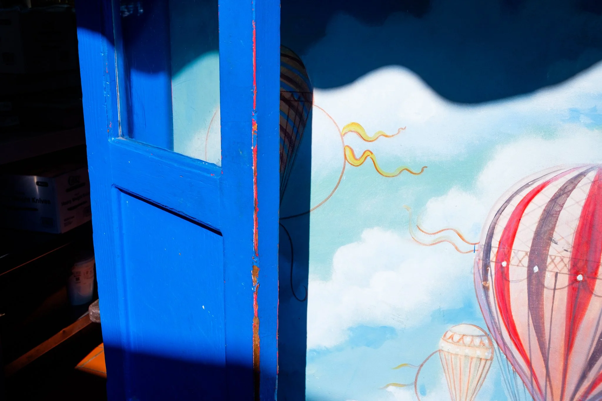 A colorful mural with part of a cartoonish face and swirling patterns, partially obscured by a blue painted wooden structure.