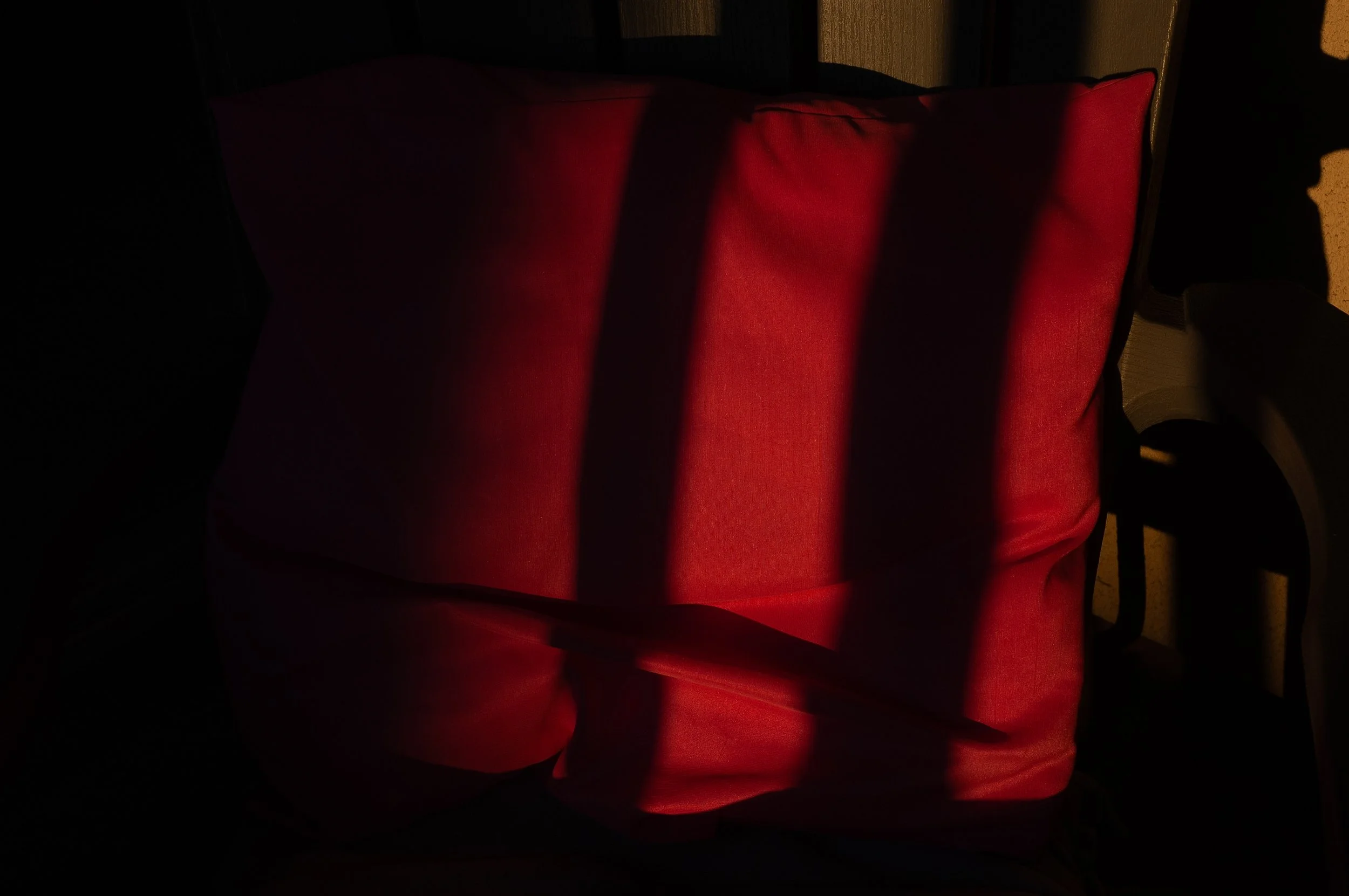 A red cushioned chair against a dark background with shadows cast across it.