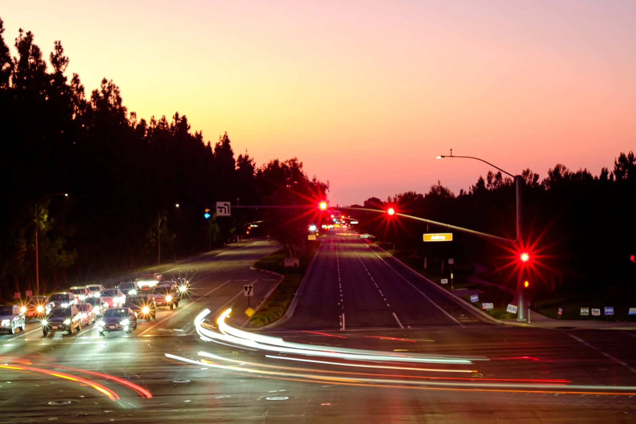 A busy road at sunset with long exposure light trails from vehicles and traffic lights.