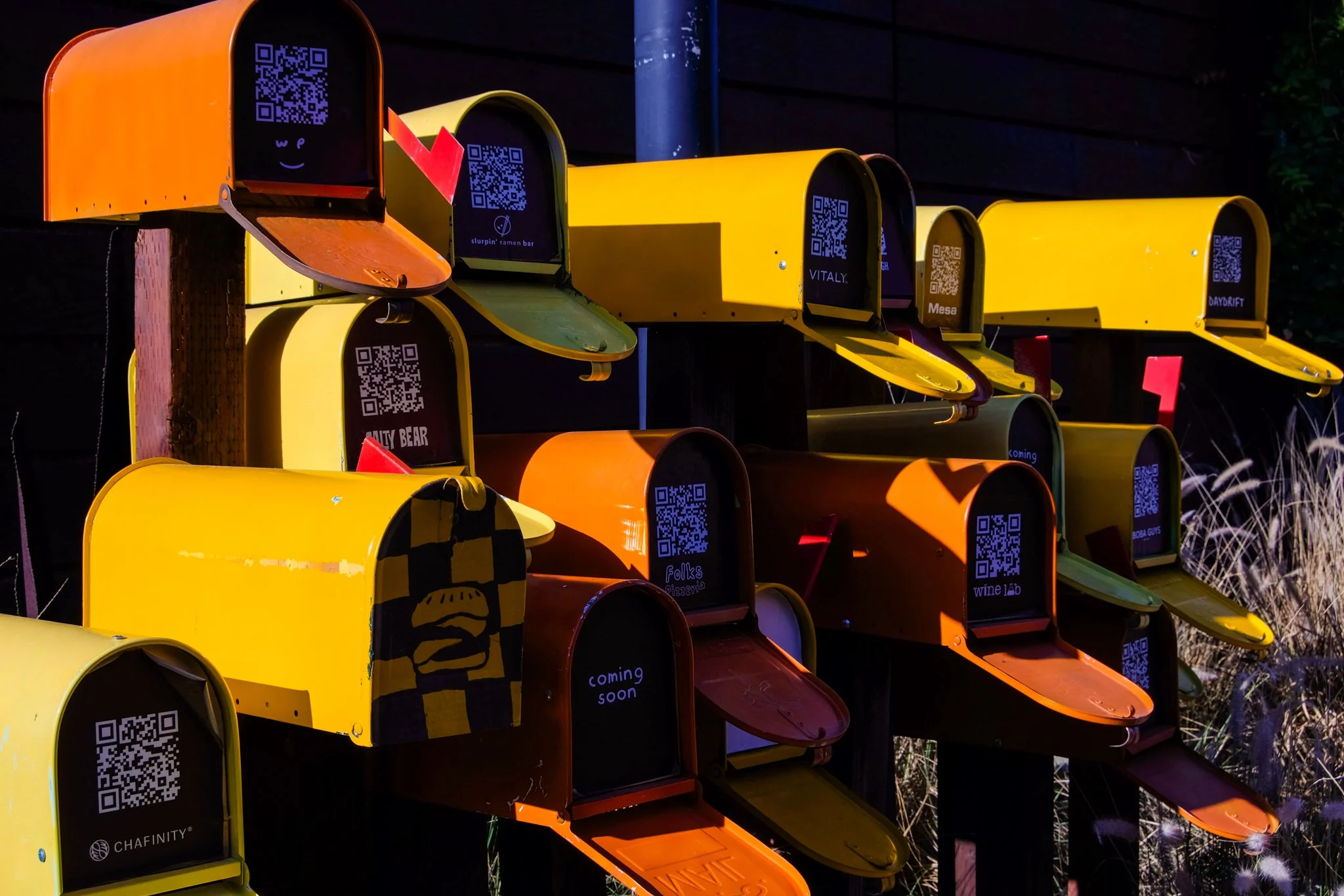 Colorful mailboxes arranged in a pattern, each with a QR code on the front and some with labels such as 'polska', 'coming soon', and 'wine lab.'
