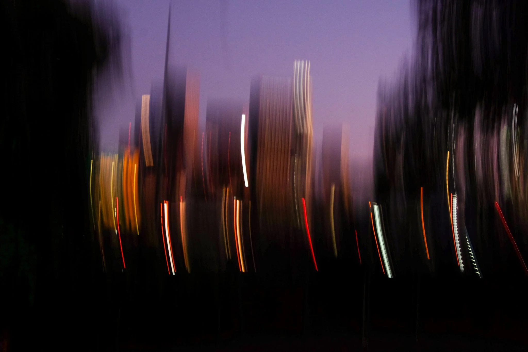 A blurry nighttime cityscape scene with tall buildings and streaks of light from moving vehicles.