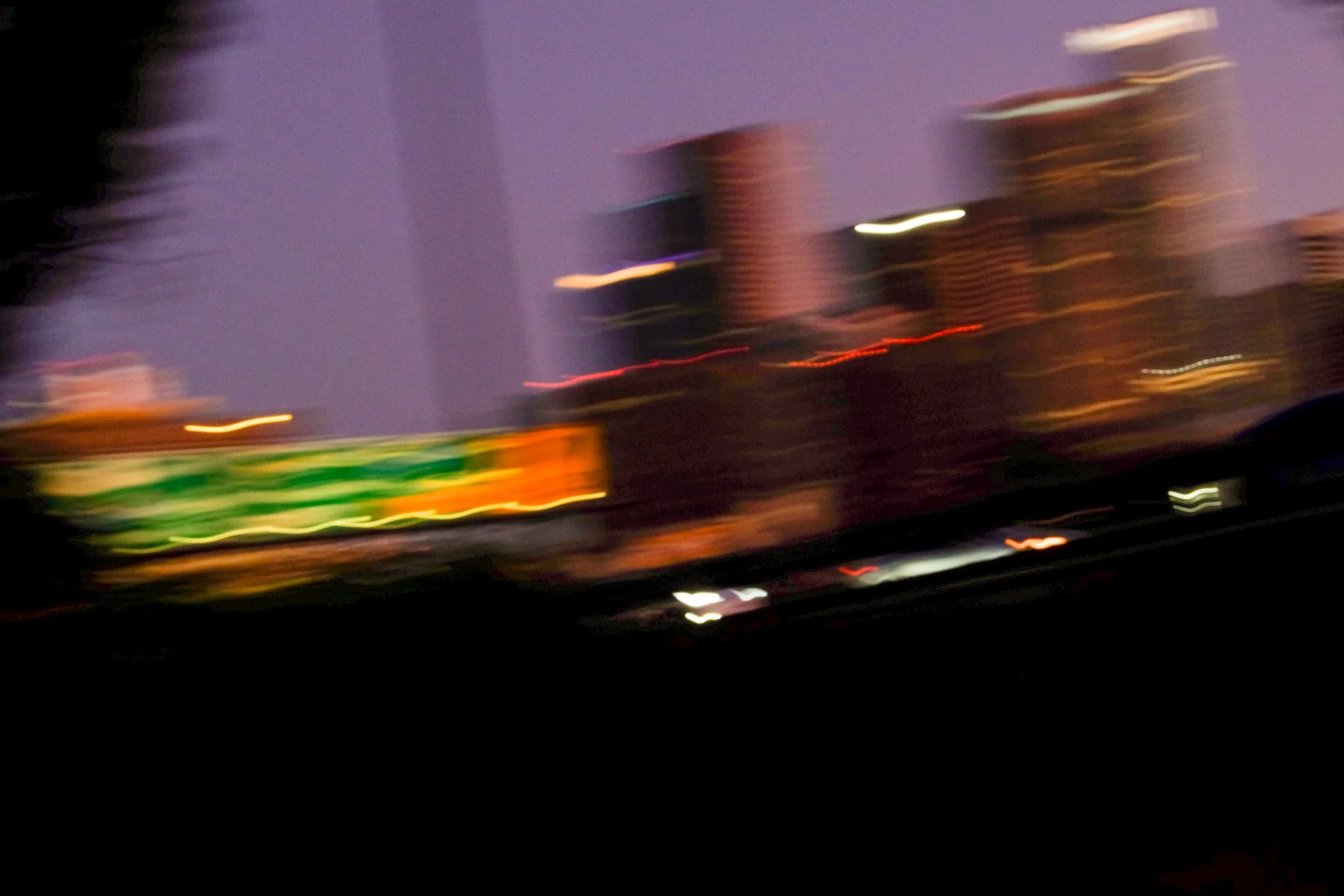 Blurred city skyline at dusk with neon and street lights.