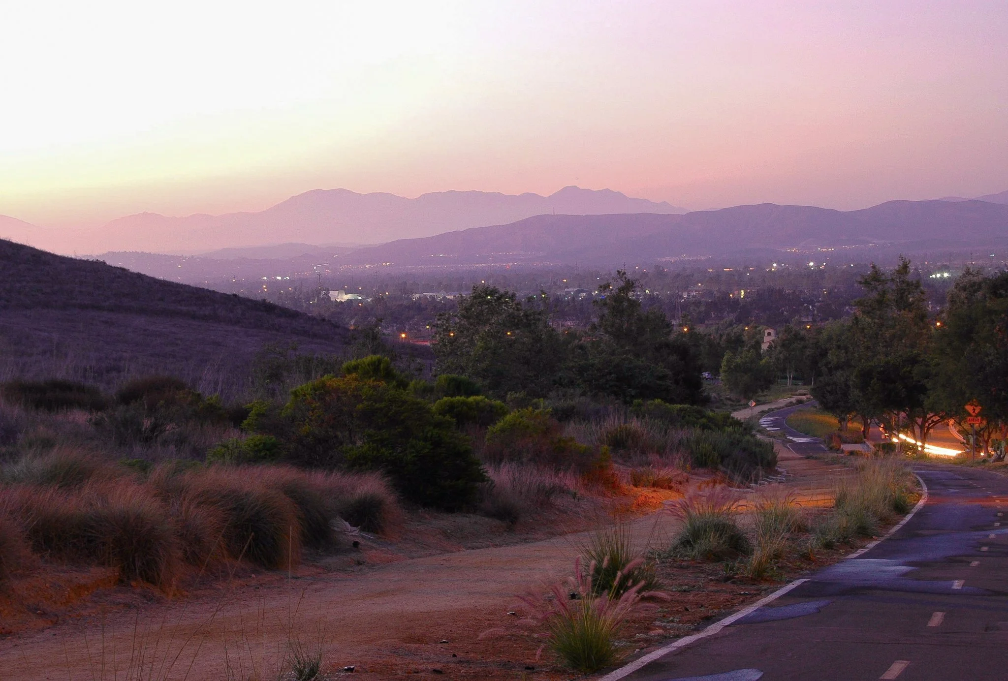 Scenic view of mountains in the distance during dusk, with a winding road and trees in the foreground.