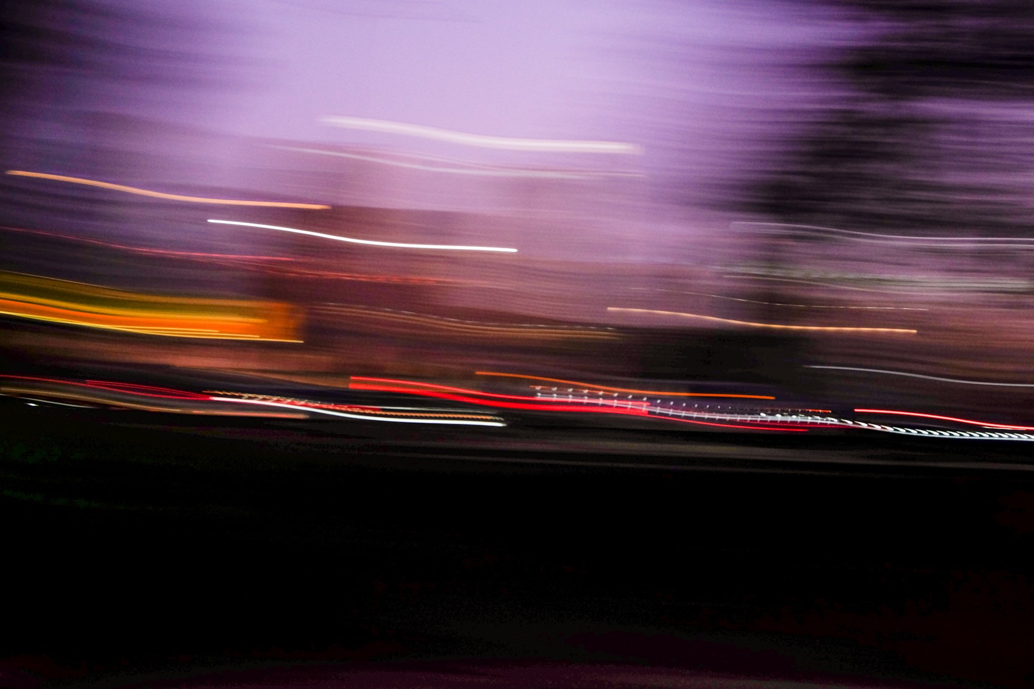 Red, white, and yellow streaks of light against a purple sky in a long exposure photograph.