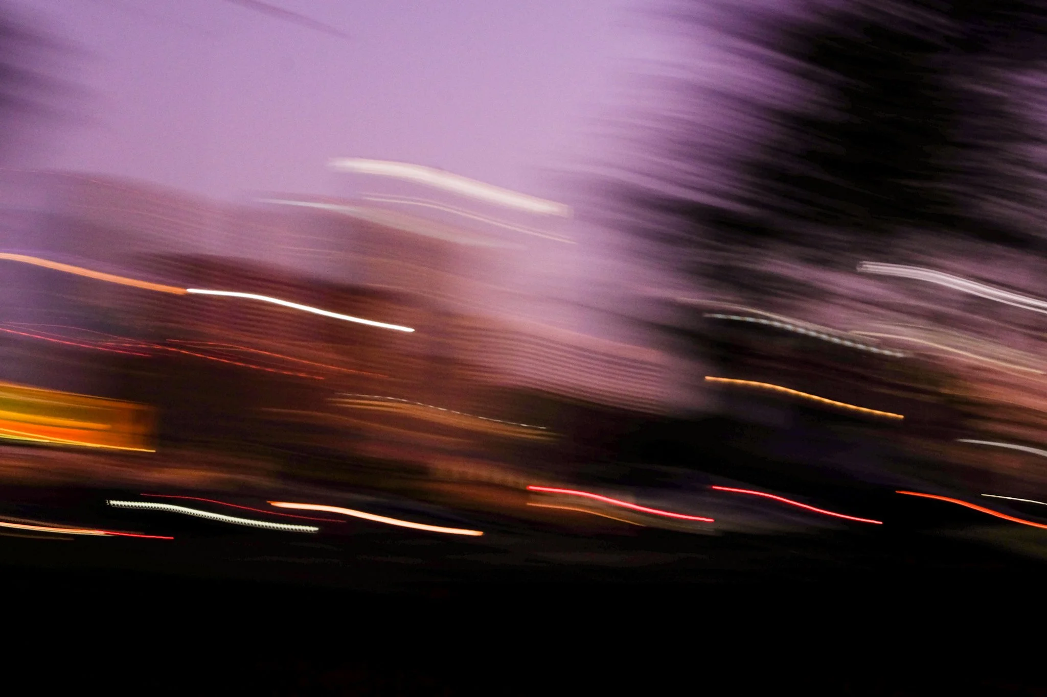 Blurred lights in motion against a dark background, with purple and black hues.