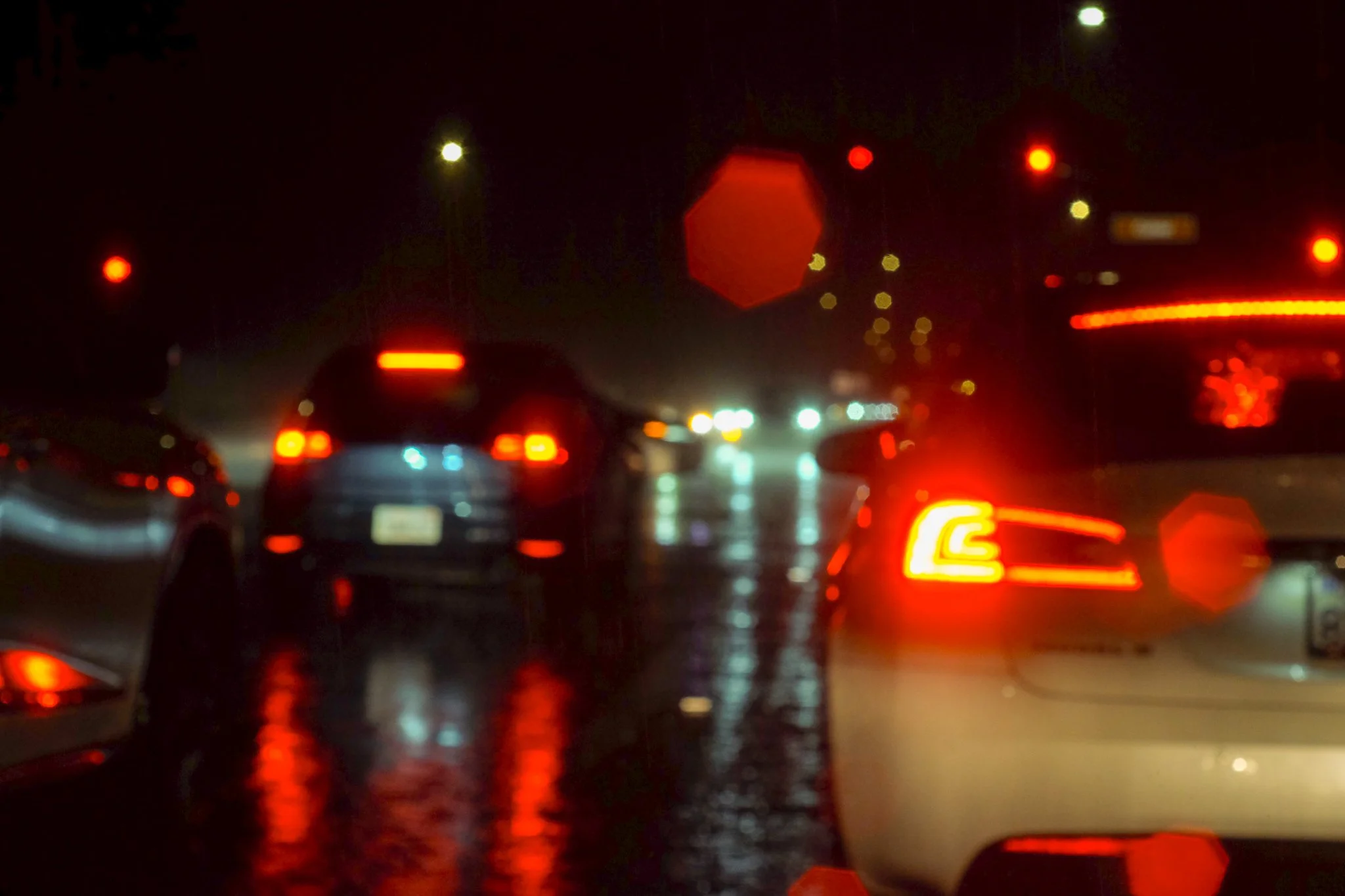 A dark, rainy night on a highway with car taillights reflecting on the wet road.