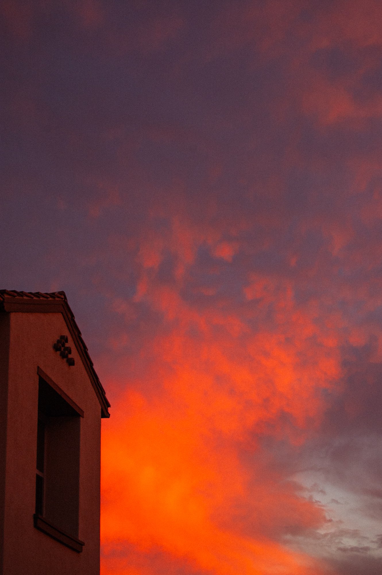 A building with a tiled roof is visible on the lower left side of the image, and the sky is filled with vibrant, colorful clouds during a sunset, showcasing shades of orange, pink, and purple.