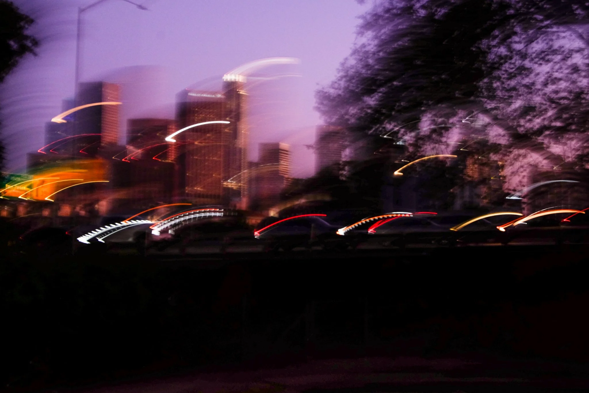 Blurry cityscape at dusk with tall buildings and lack of focus causing streaked lights and indistinct features.