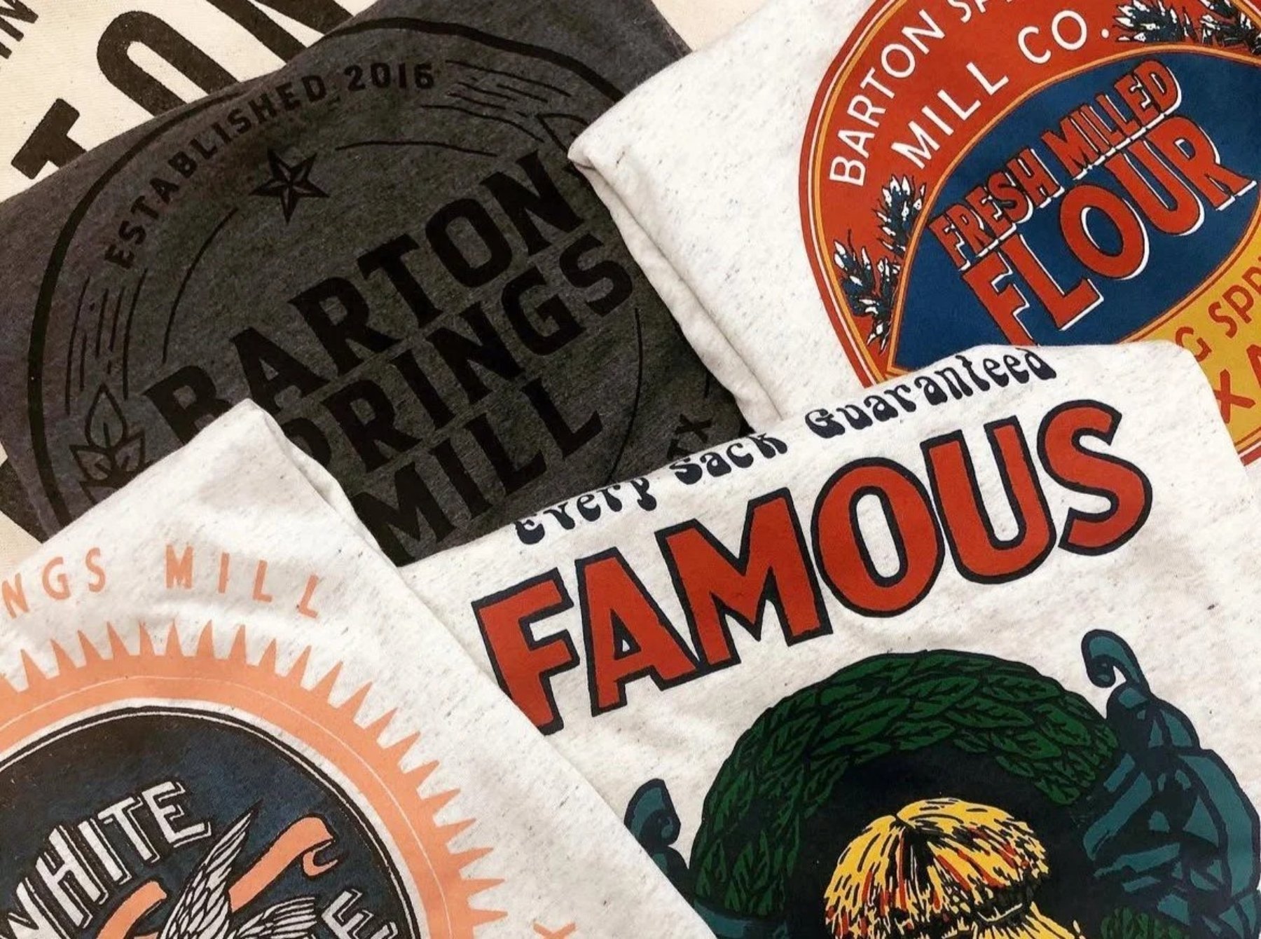 Custom screen printed shirts folded and stacked in frame for Barton Springs Mill Austin Texas Business.