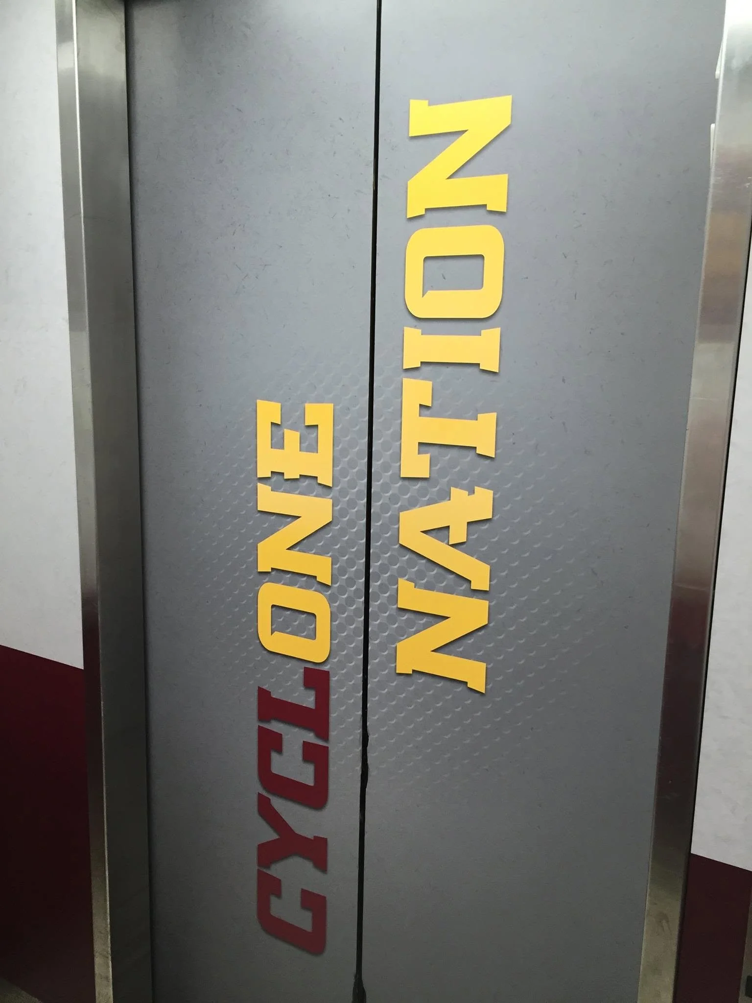 An elevator door with yellow and red text that is partially visible, reading 'WELCOME' vertically.