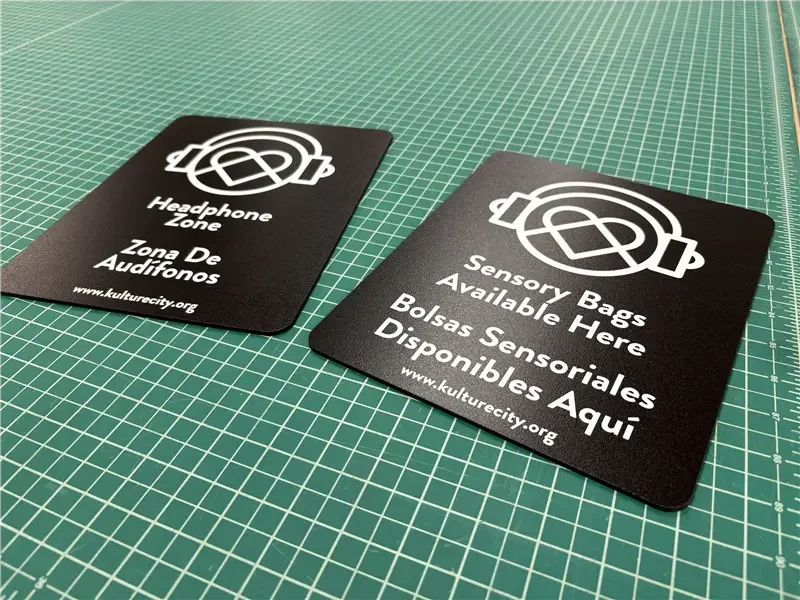 Two black sign cards on a green cutting mat, one indicating a headphone zone and the other for sensory bags available at www.kulturecity.org.
