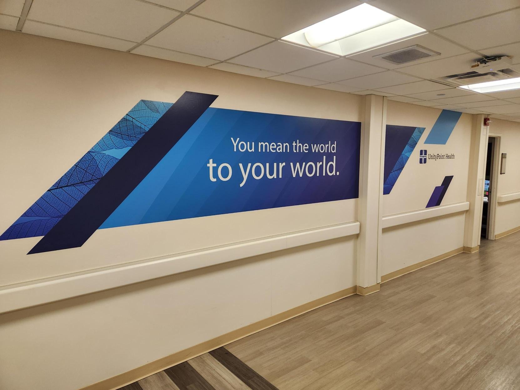 Interior hallway wall featuring a blue and purple geometric mural with the text 'You mean the world to your world.' and a logo for UnityPoint Health.
