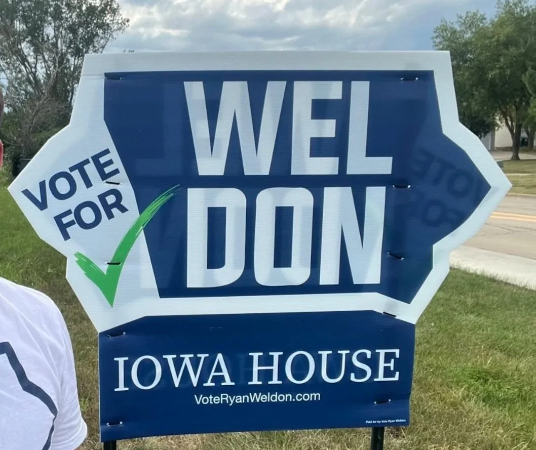 Political campaign sign supporting Ryan Weldon for Iowa House with a slogan 'Wel Don' and a 'Vote for' sticker with a checkmark.