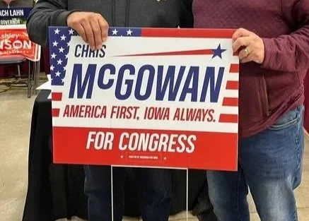 Sign held by a person promoting Chris McGowan for Congress, featuring patriotic colors and design with text: "Chris McGowan, America First, Iowa Always, For Congress."