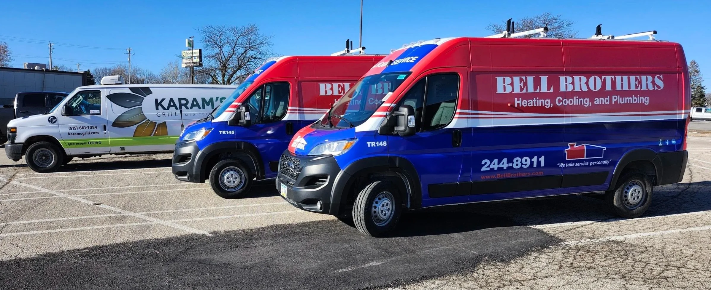 A parking lot with three service trucks, two branded 'Bell Brothers' and one 'Karam's Grill,' under a clear blue sky with some trees and signage in the background.