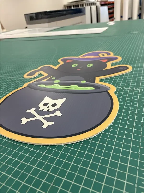 A Halloween-themed sticker of a black cat wearing a purple witch hat, sitting behind a bubbling cauldron with a skull and crossbones symbol.
