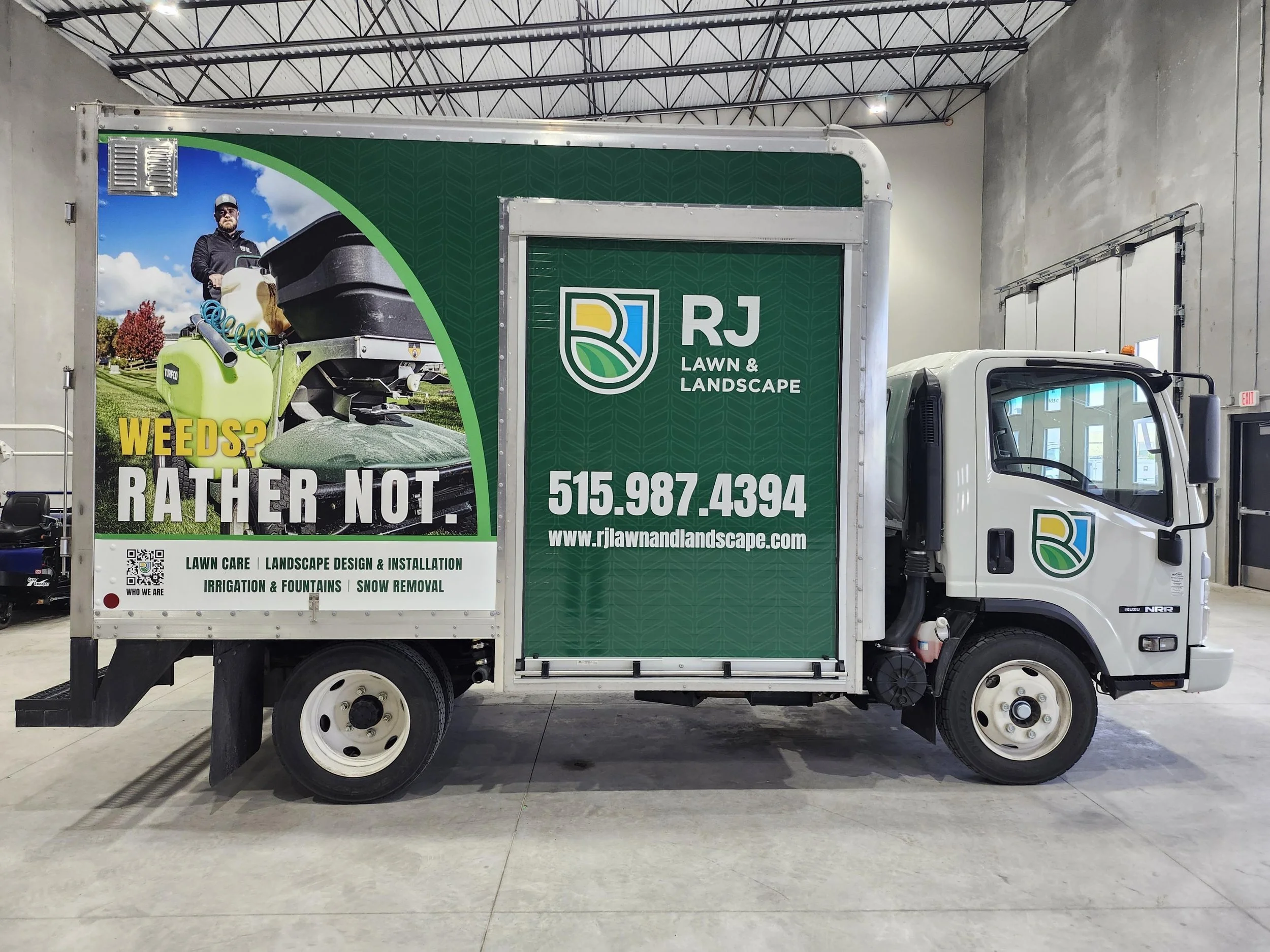 A white lawn care truck with a green and white advertisement on the side. The advertisement features a man operating lawn equipment and text for 'RJ Lawn & Landscape,' including a website and phone number.
