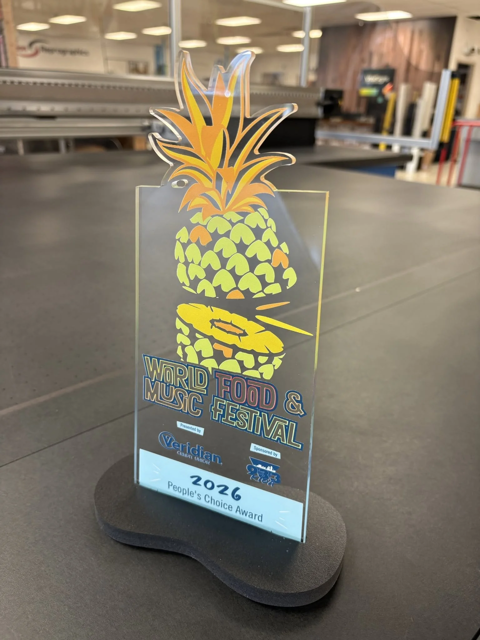 Acrylic award for the 2026 World Food & Music Festival on a black freestanding signboard with colorful pineapple graphic.