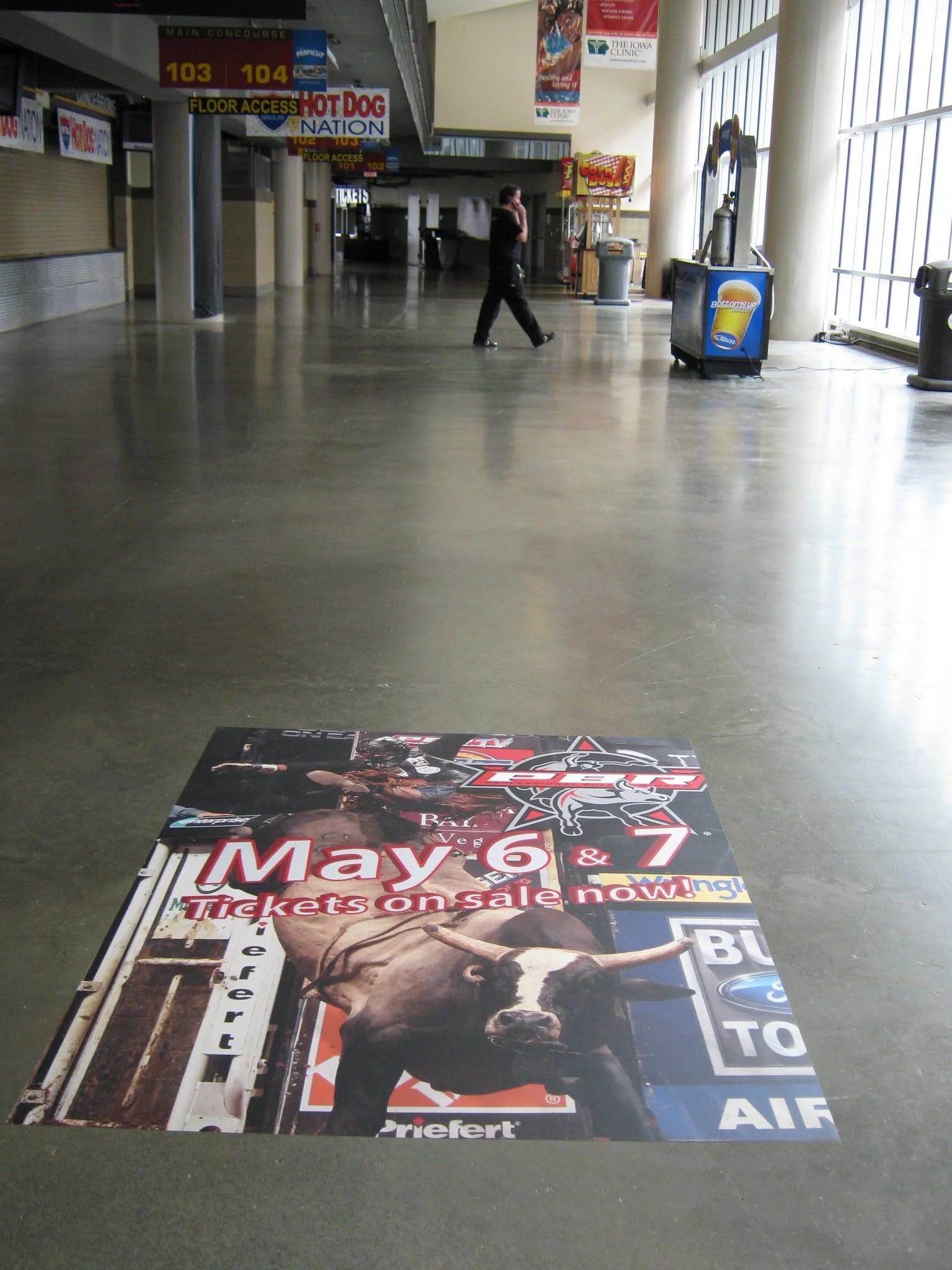 Large colorful advertising poster on the floor promoting ticket sales for May 6 and 7, with images of race cars and bold text highlighting the dates and ticket sale information.