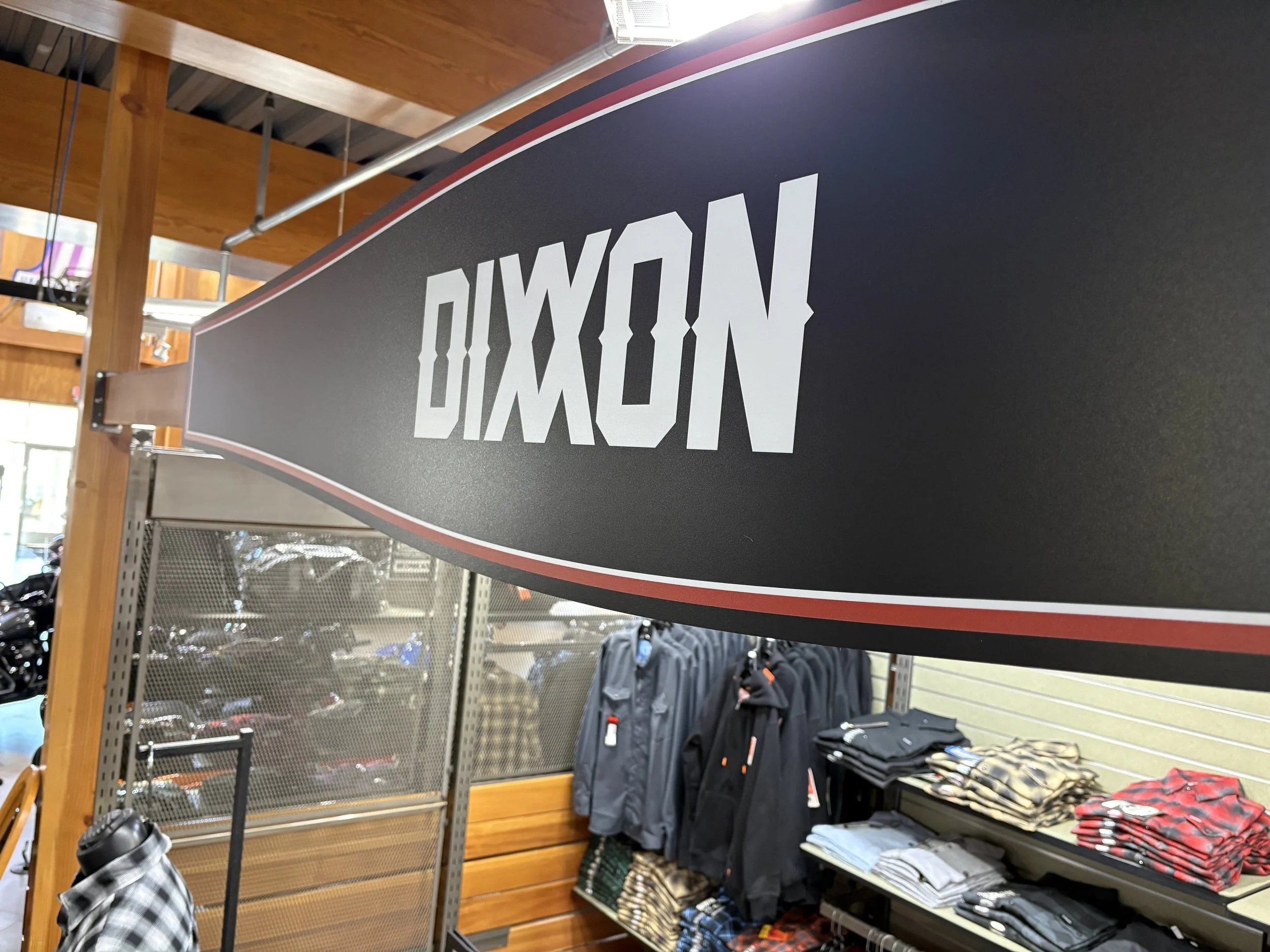 A retail store display with a large sign reading 'Men' in bold white letters on a black background, surrounded by clothing racks, folded clothes, and other retail fixtures.