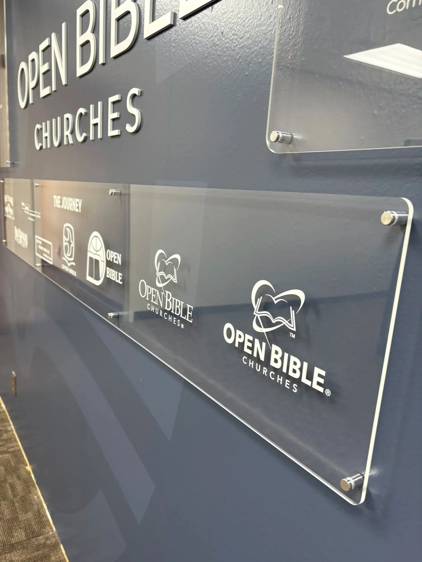 Part of an acrylic display for Open Bible Churches with the text 'Open Bible Churches' and logo, mounted with satin silver standoffs.