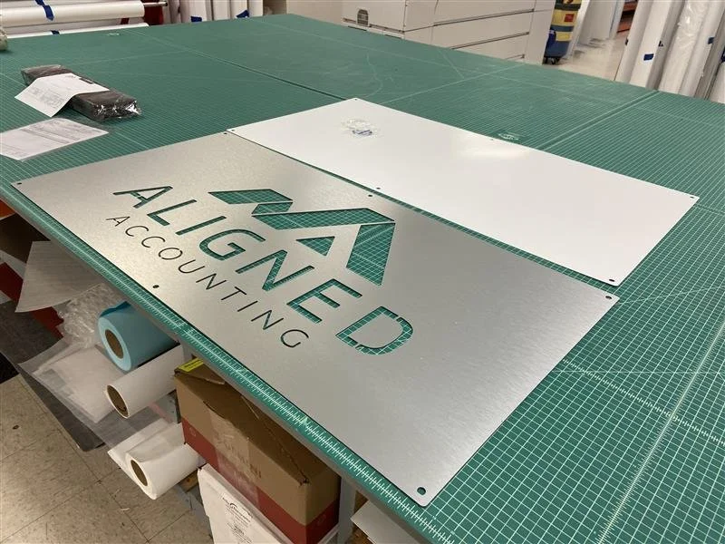 Metal sign with the logo and text 'ALIGNED ACCOUNTING' on a green worktable in a workshop.