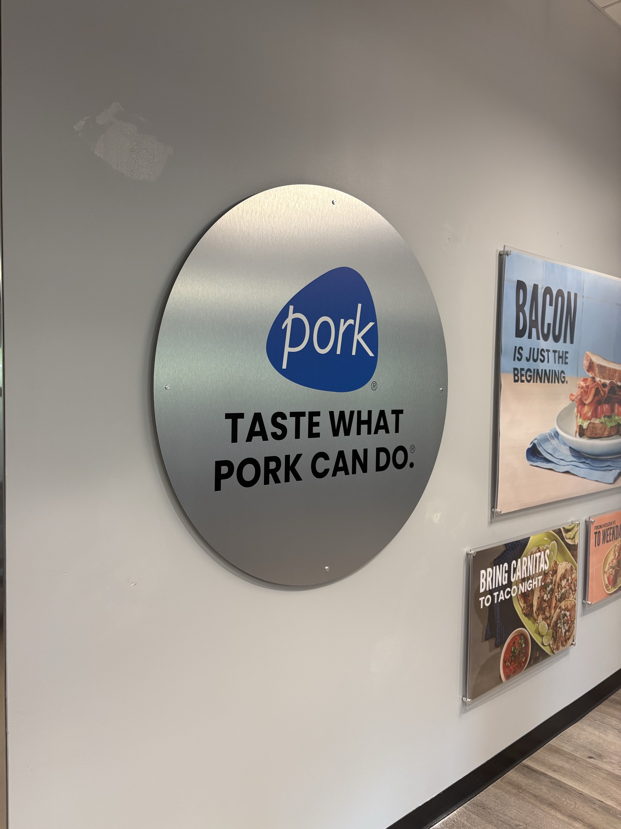 Restaurant sign displaying the word 'pork' with the phrase 'Taste what pork can do.' The sign is mounted on a white wall near a menu display.