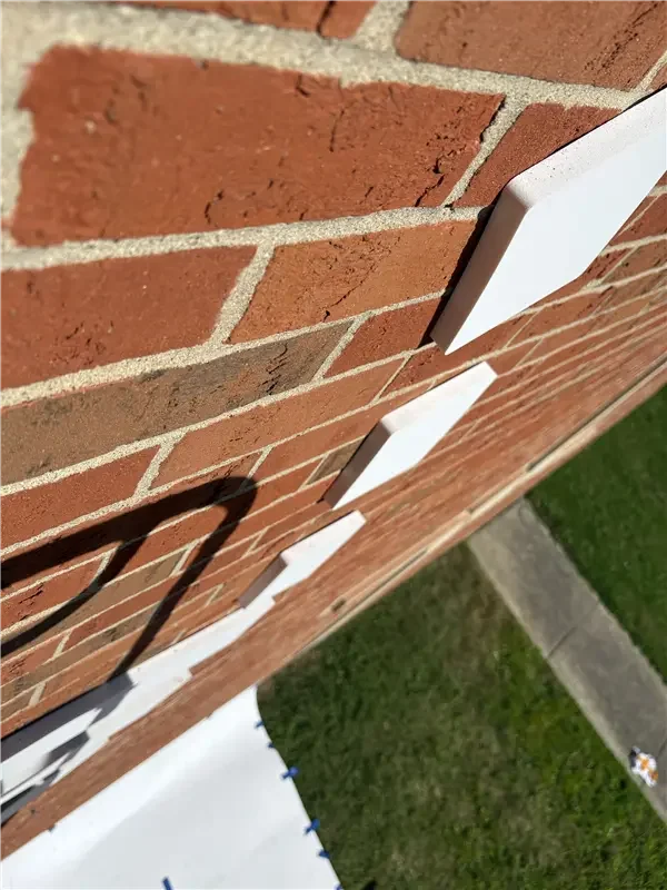 Close-up of a brick wall with white utility boxes attached, cast shadow on the wall, and a grassy area below.