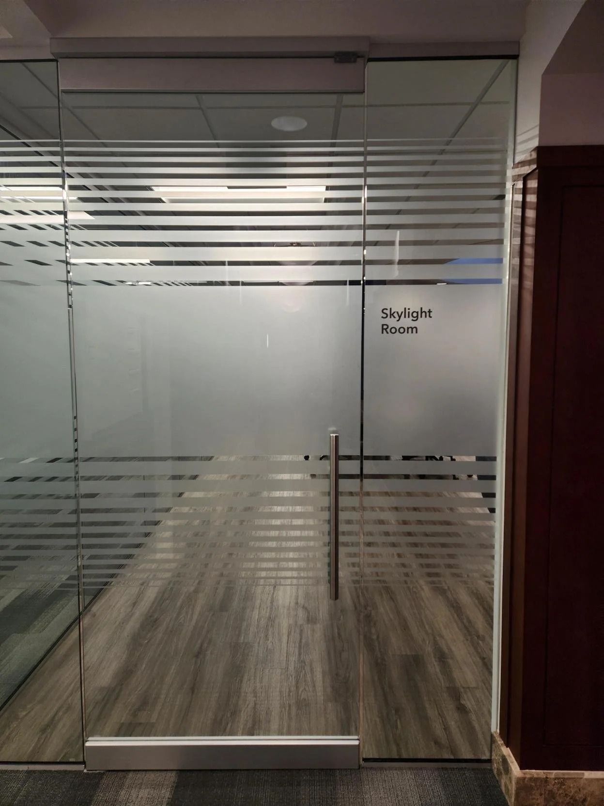 Glass door with the text "Skylight Room" written on it, leading into a room with striped glass panels and wooden flooring.