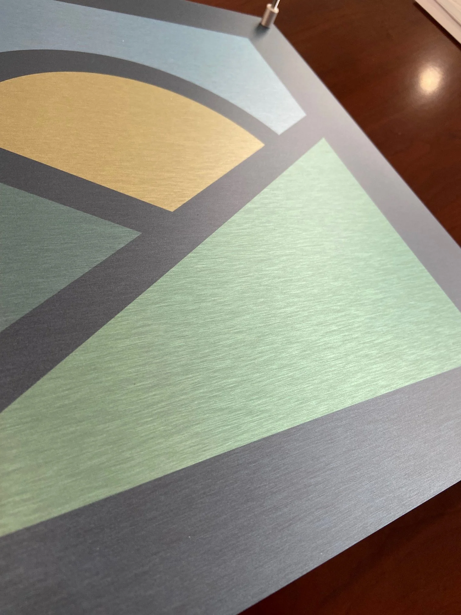 Close-up of a colorful abstract geometric pattern on a flat surface, with shades of green, yellow, gray, and brown.