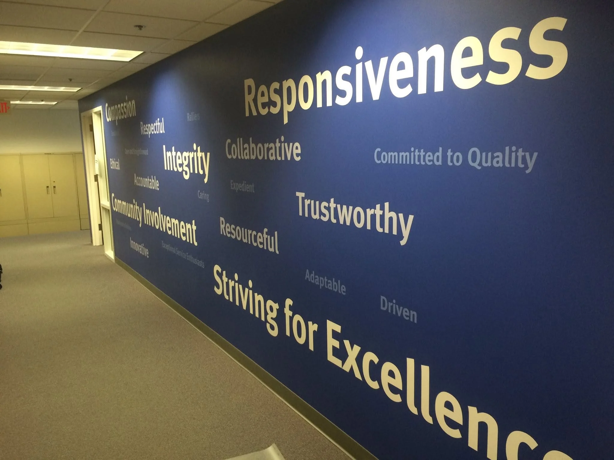 Blue wall with white and yellow words including responsibility, integrity, community involvement, striving for excellence, and ethical.