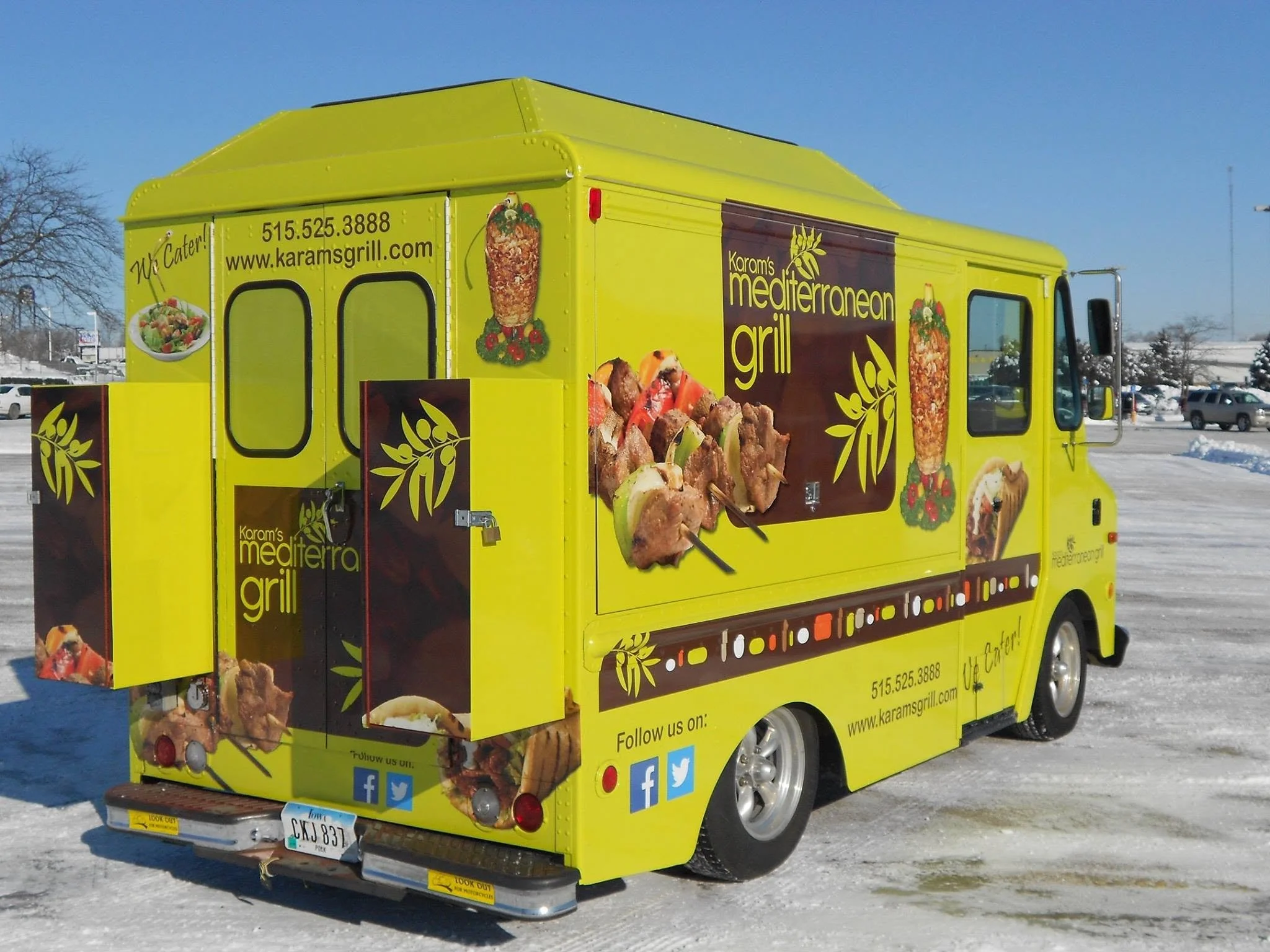 Yellow food truck advertising Mediterranean grill, with images of grilled meat, vegetables, and skewers, parked outdoors in a snowy area.