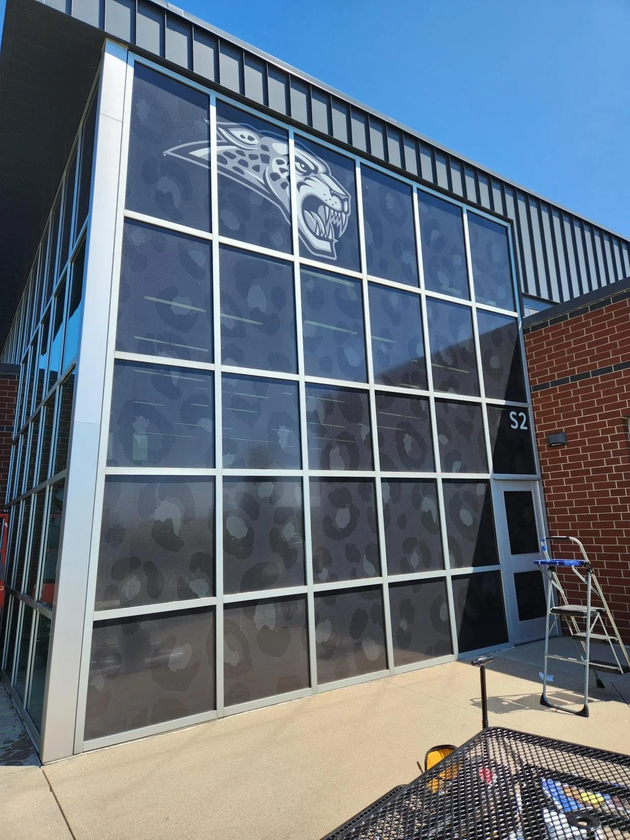 Exterior view of a modern glass building with the Jacksonville Jaguars logo on the window. Ladder and equipment are nearby.