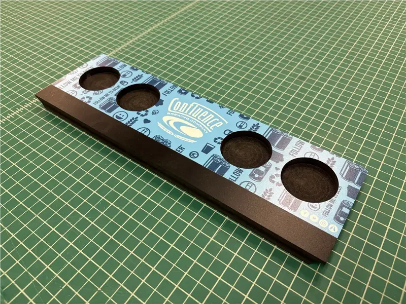 A rectangular cannabis concentrate tray with four circular cavities, decorated with cannabis-themed graphics and logo, placed on a green grid cutting mat.