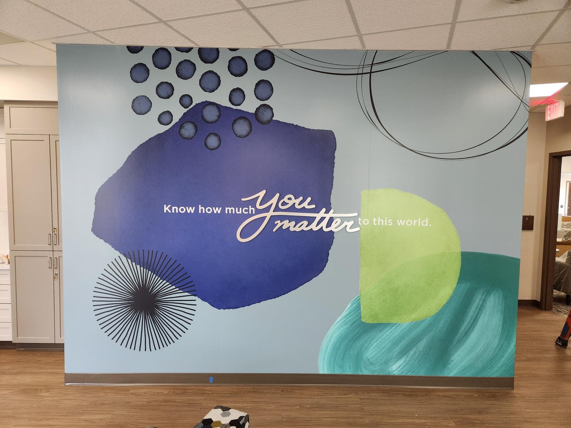 Decorative wall with abstract shapes, including blue and yellow blobs, black circles with radiating lines, and curved lines, with the partially visible text 'Know how much you matter'.