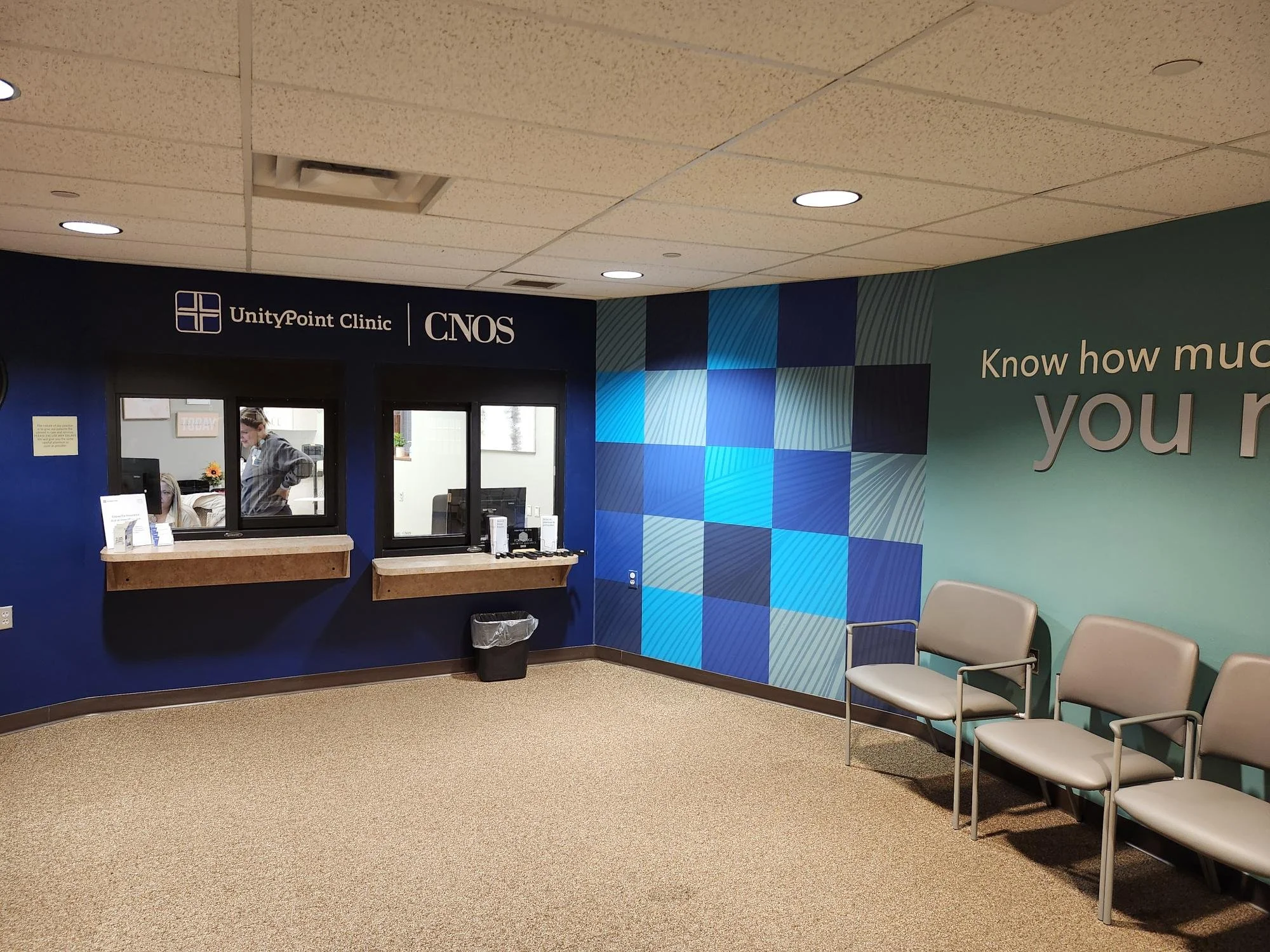 Reception area at UnityPoint Clinic with chairs, a wall with blue geometric design, and a windowed check-in counter.