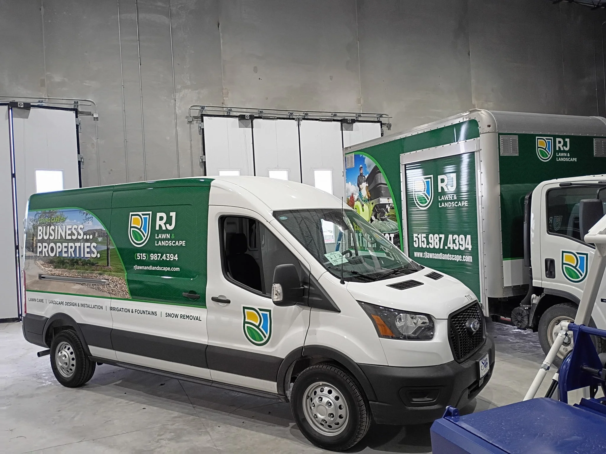 Green and white RJ Lawn & Landscape service vans parked indoors, with company branding, contact info, and images of landscape services.