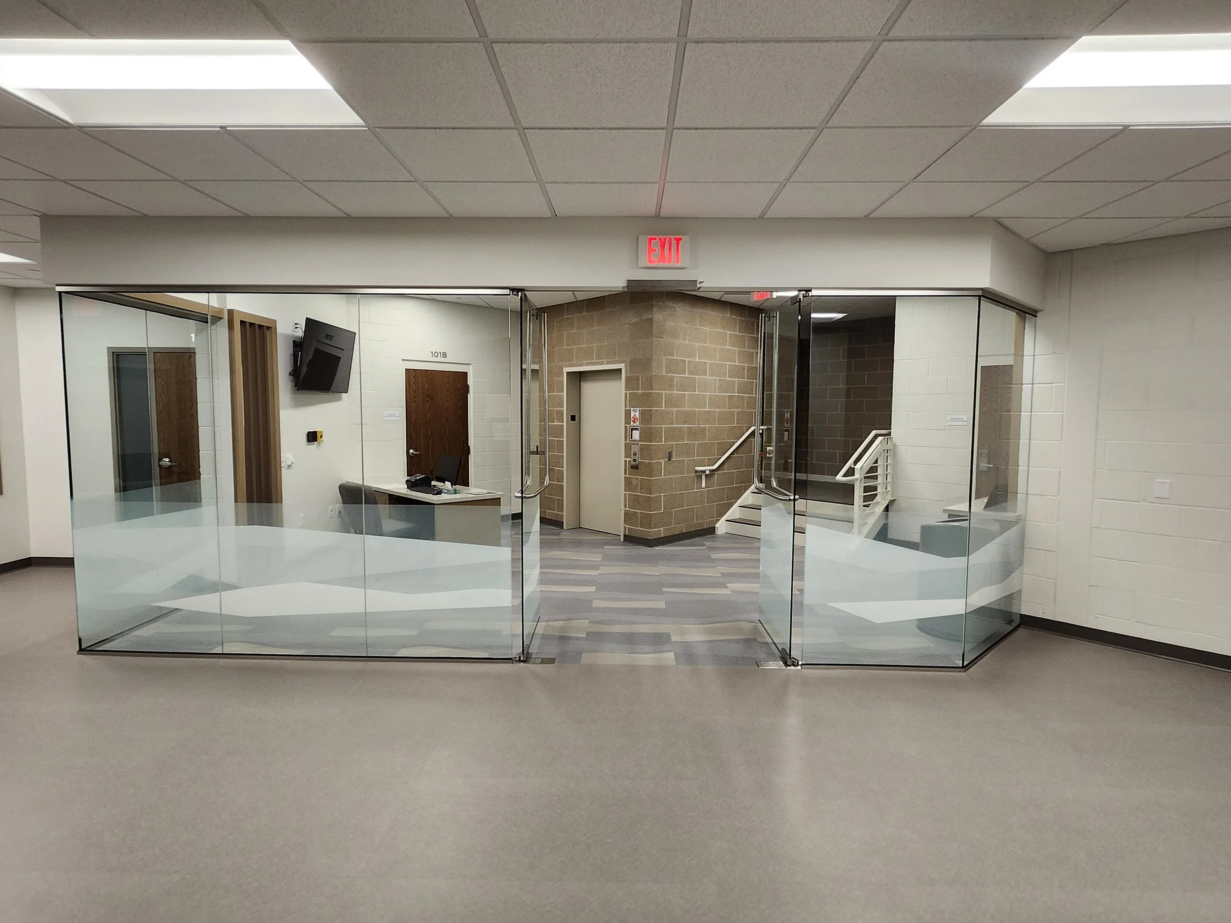 Entrance to an office building with glass doors, a reception area visible inside, and an exit sign above the doorway.