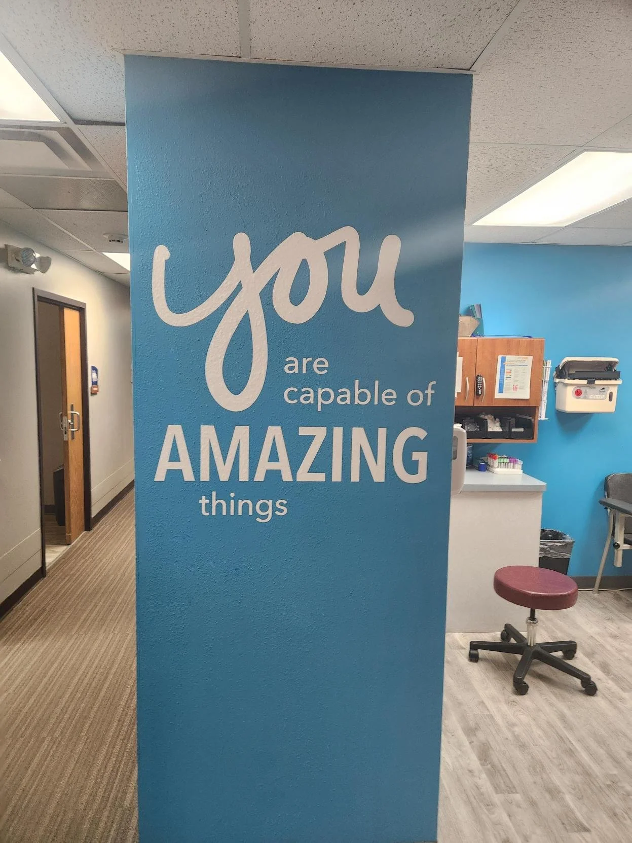 A blue wall with white text that reads 'you are capable of AMAZING things' inside a medical or office setting.