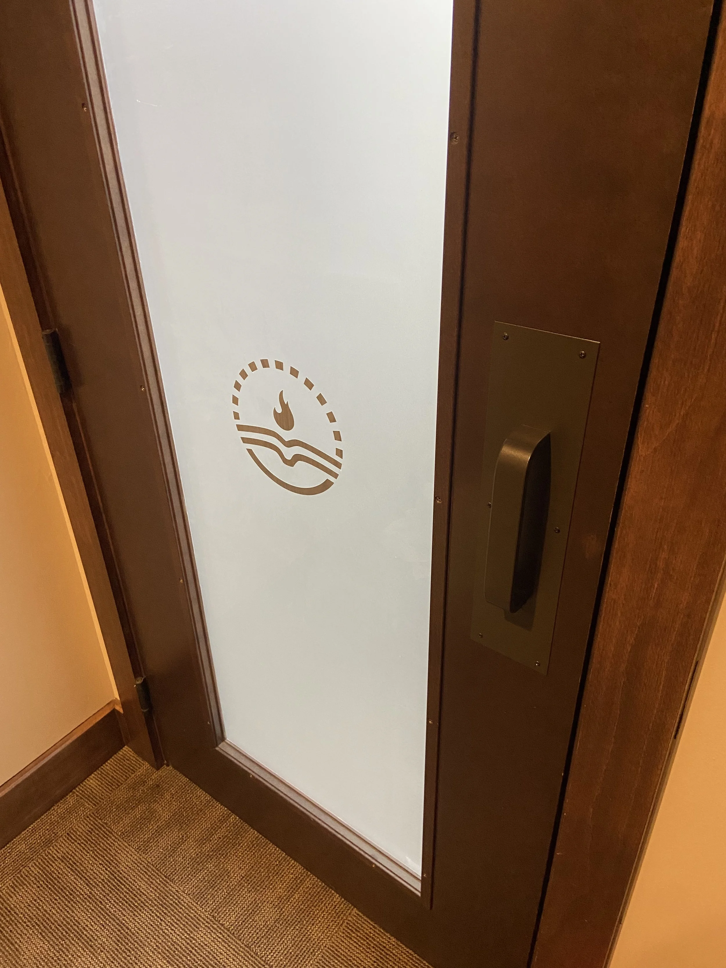 Elevator door with a sticker of a hand with a flame on top and a wave below, indicating a no-touch or no-smoking symbol.